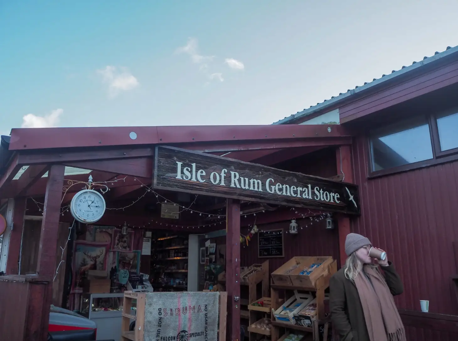 The writer wearing a scarf and hat and sipping a to-go coffee outside the Isle of Rum General Store.