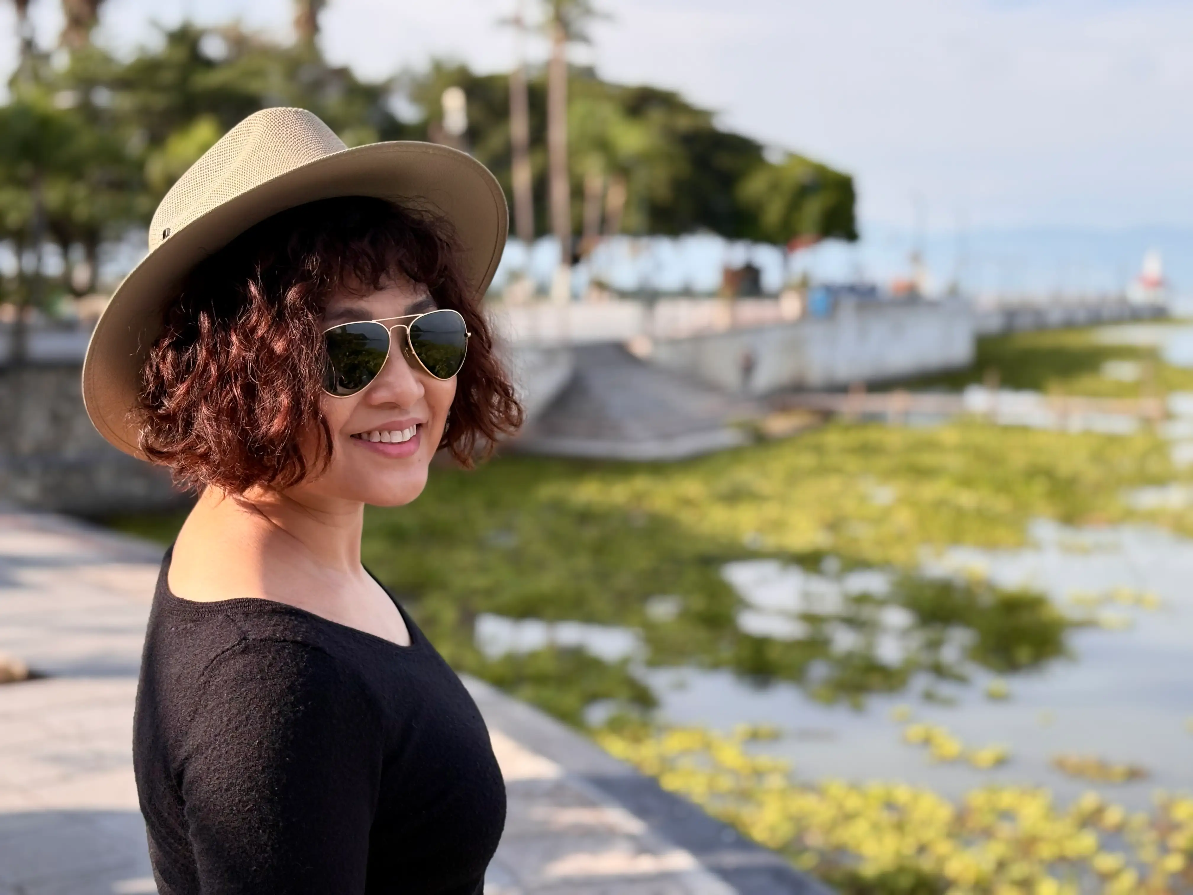 Woman smiling in front of water with hat on