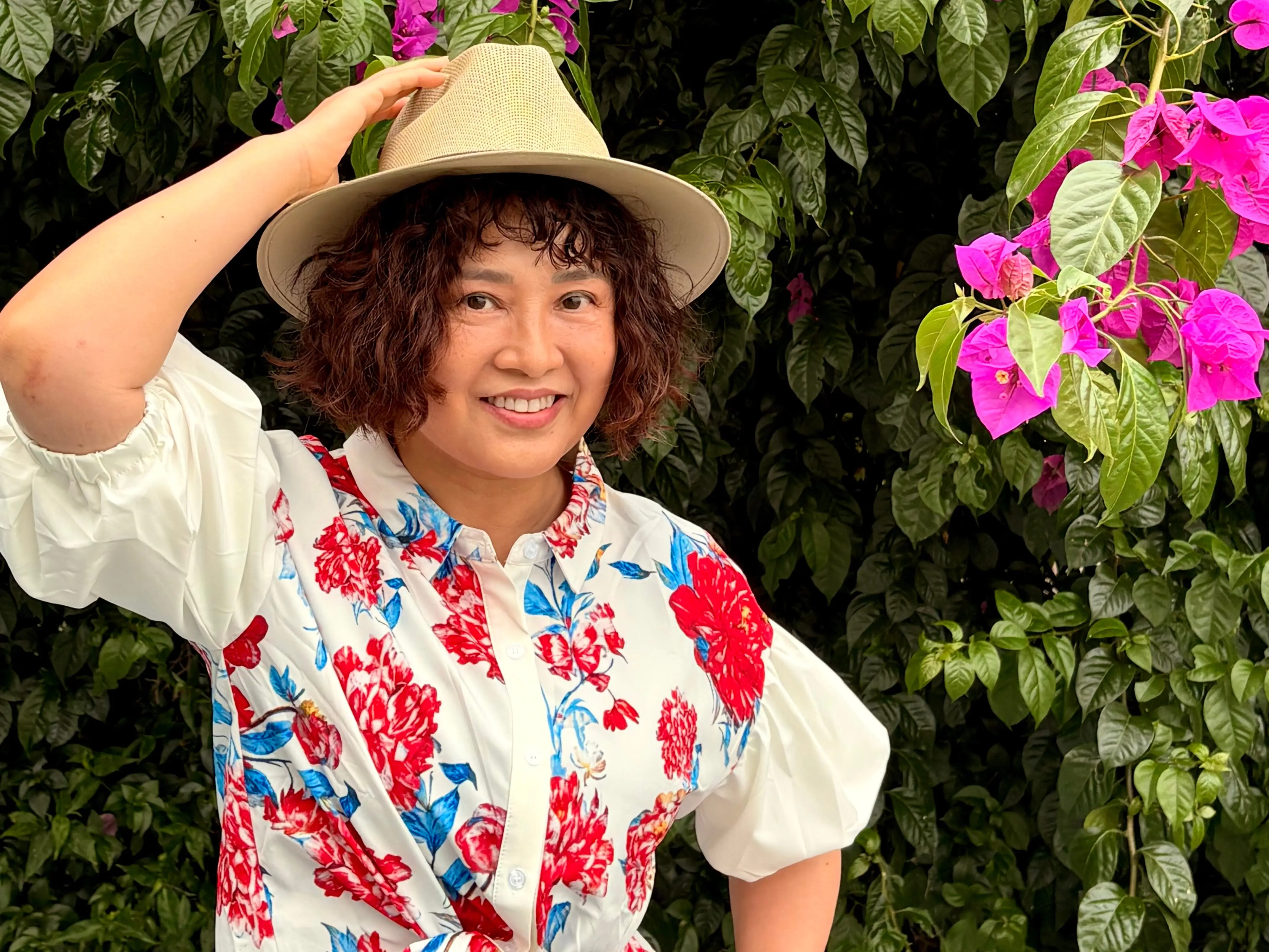 Woman with hat on smiling near greenery