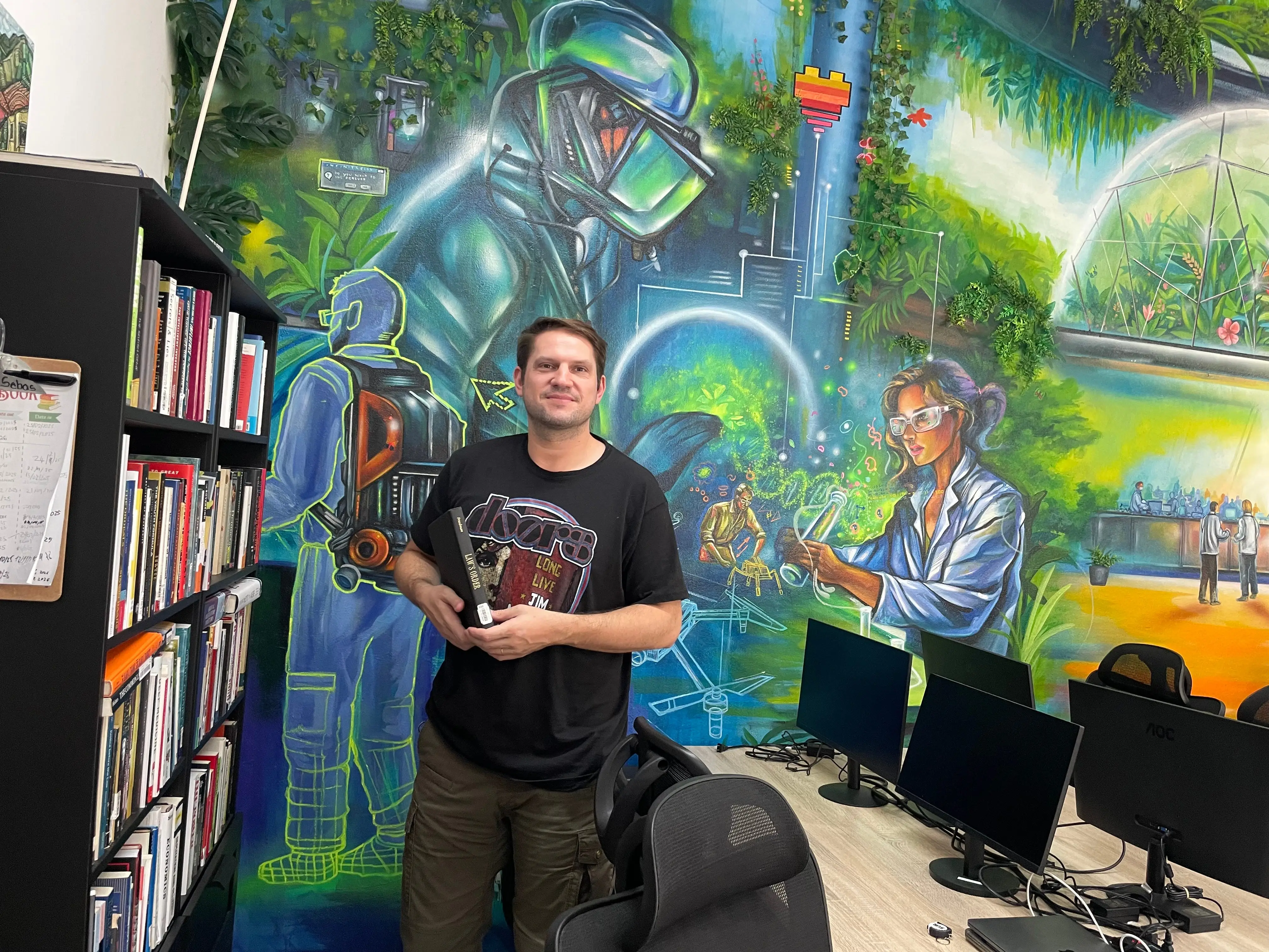 Niklas Anzinger stands next to a bookshelf.