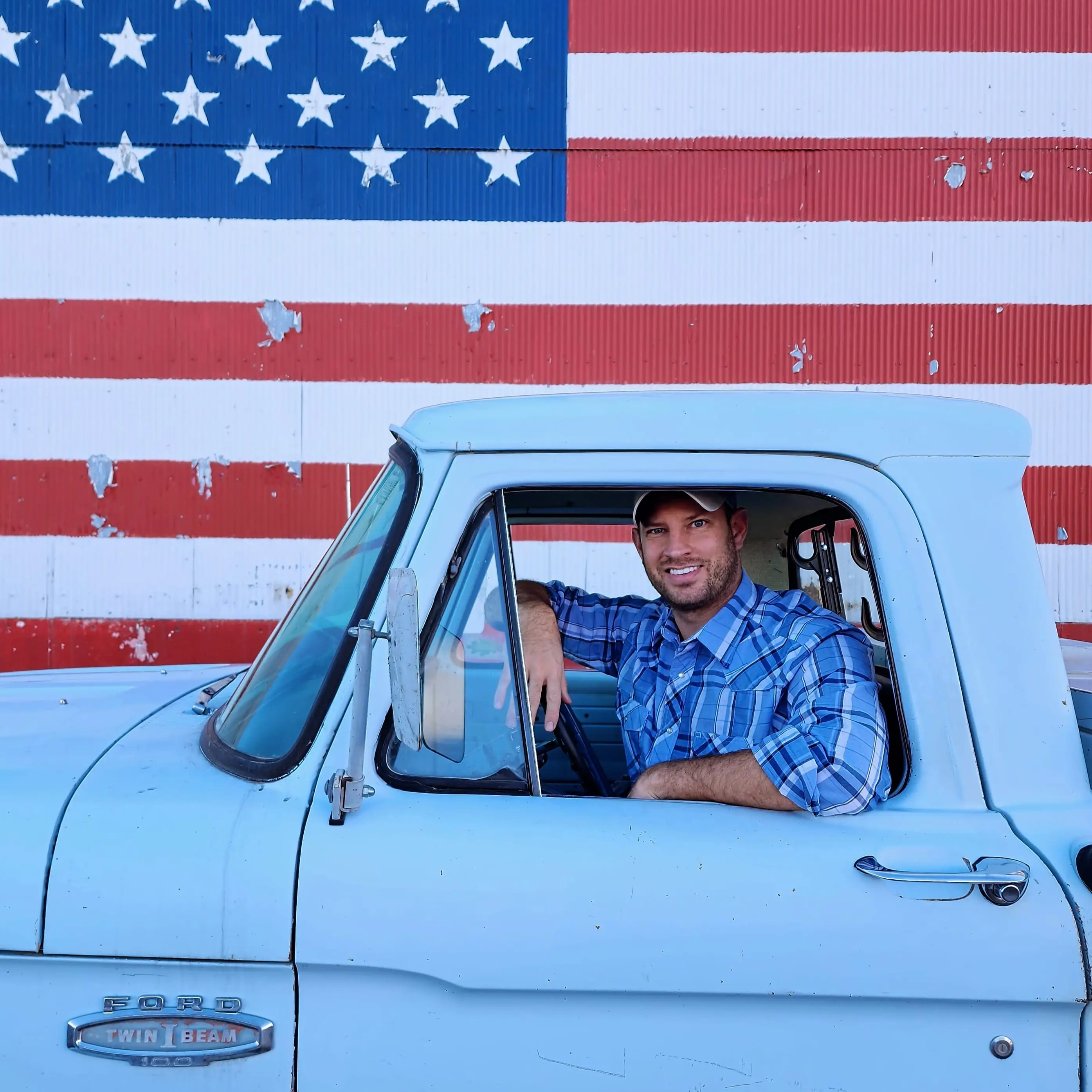 Montana Senator Kenneth Bogner sits in a Ford pickup truck in front of an American flag mural.