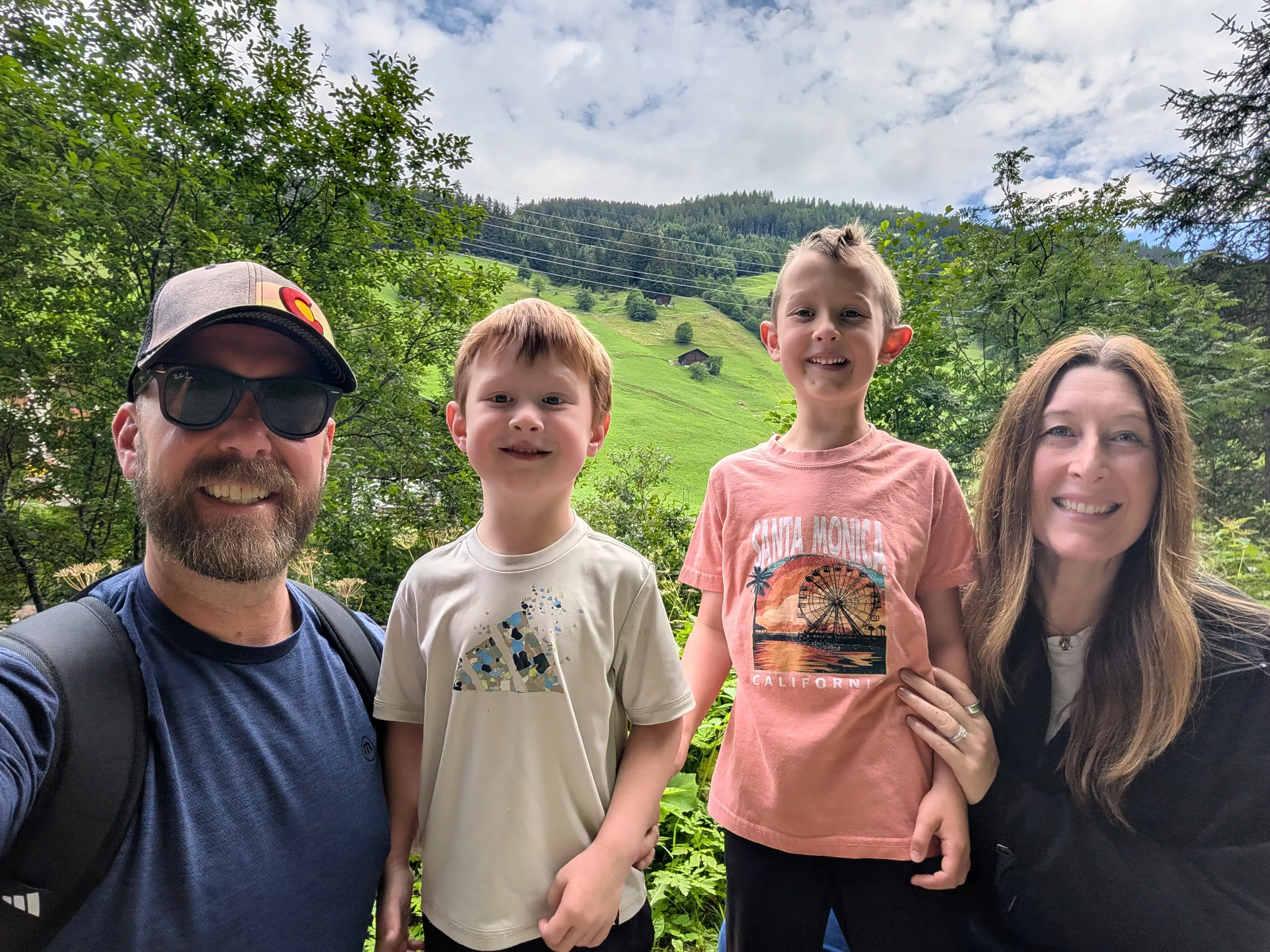 Family of four smiling in front of trees