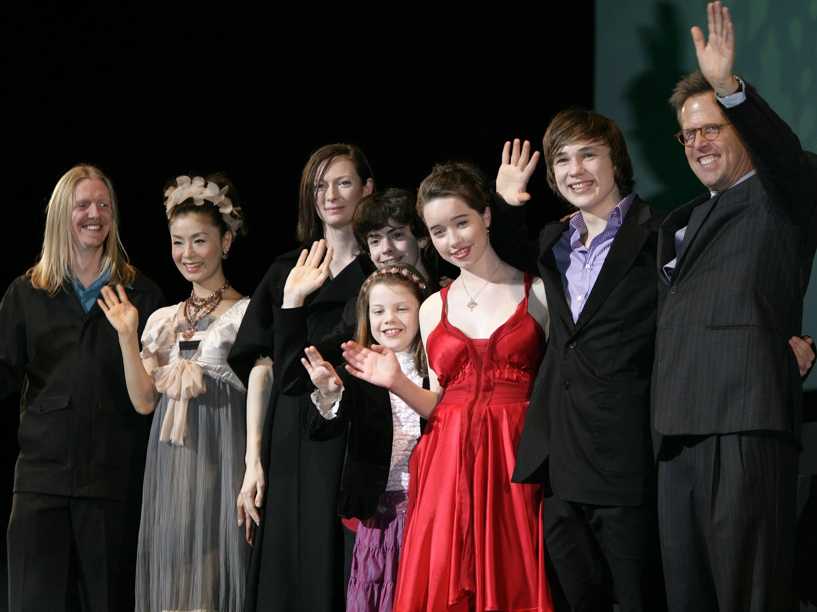 Several people wave to a crowd at a movie premiere.