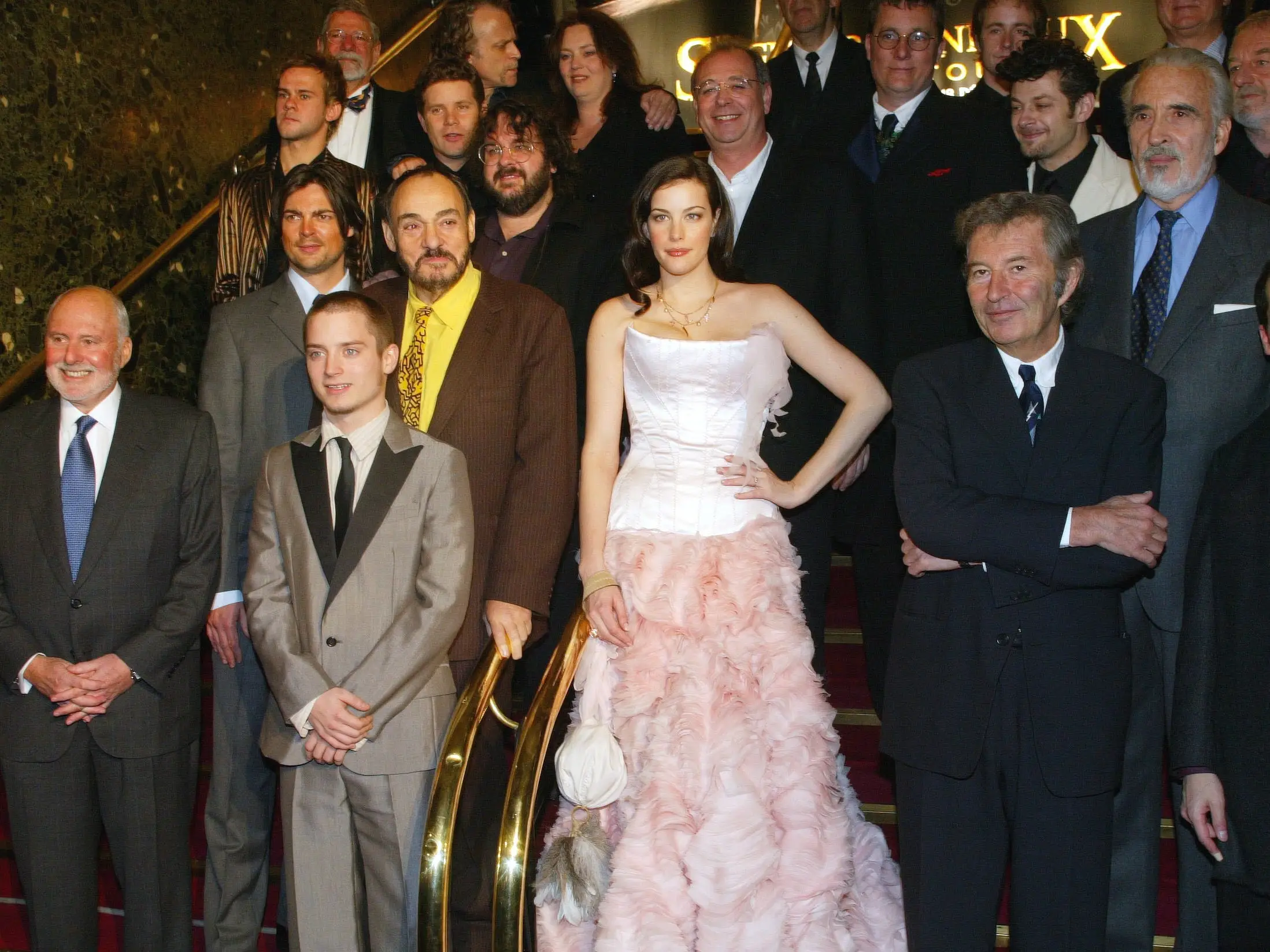 Several actors pose for a photo on a red carpet staircase.
