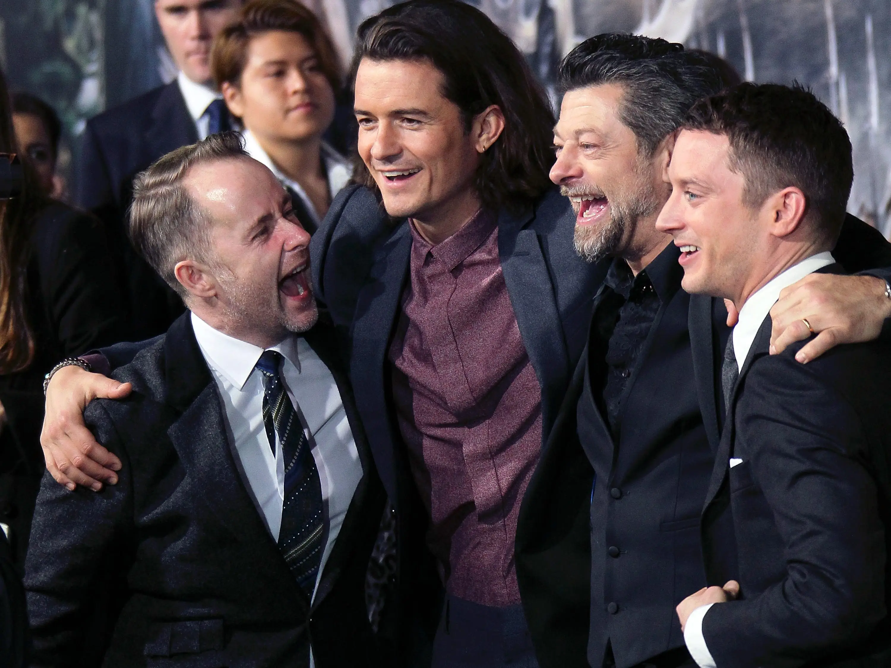 Four actors in tuxedos laugh and pose for a photo.