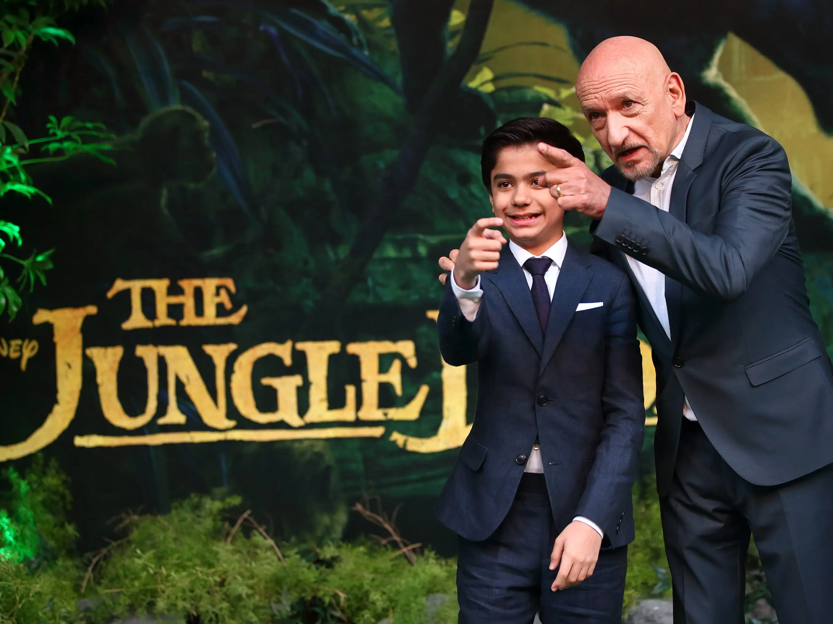 Two actors in navy suits pose for a photo at a movie premiere.