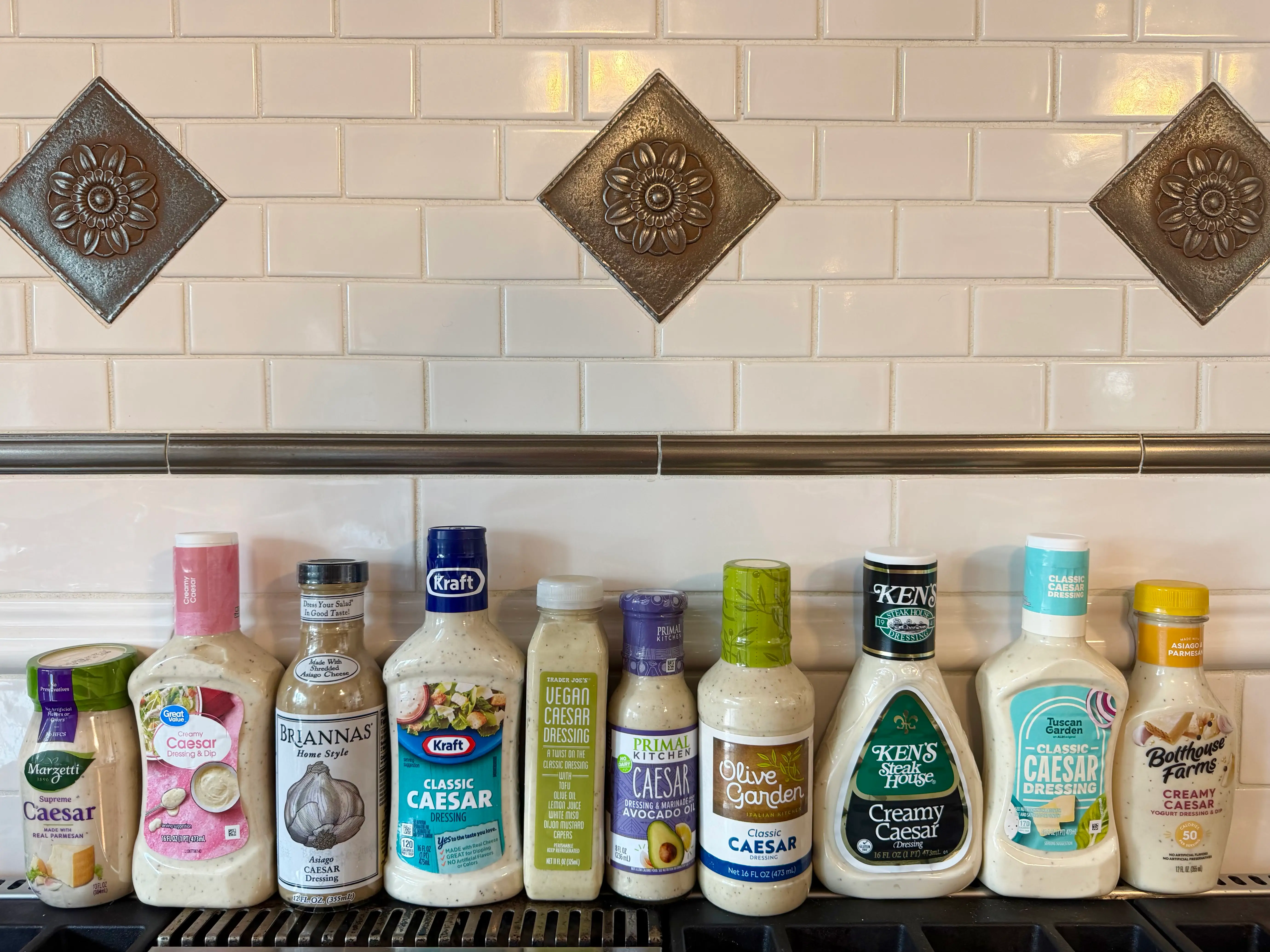 Marzetti, Great Value, Brianna's, Kraft, Trader Joe's, Primal Kitchen, Olive Garden, Ken's Steak House, Aldi's Tuscan Garden, and Bolthouse Farms Caesar dressings lined up on counter