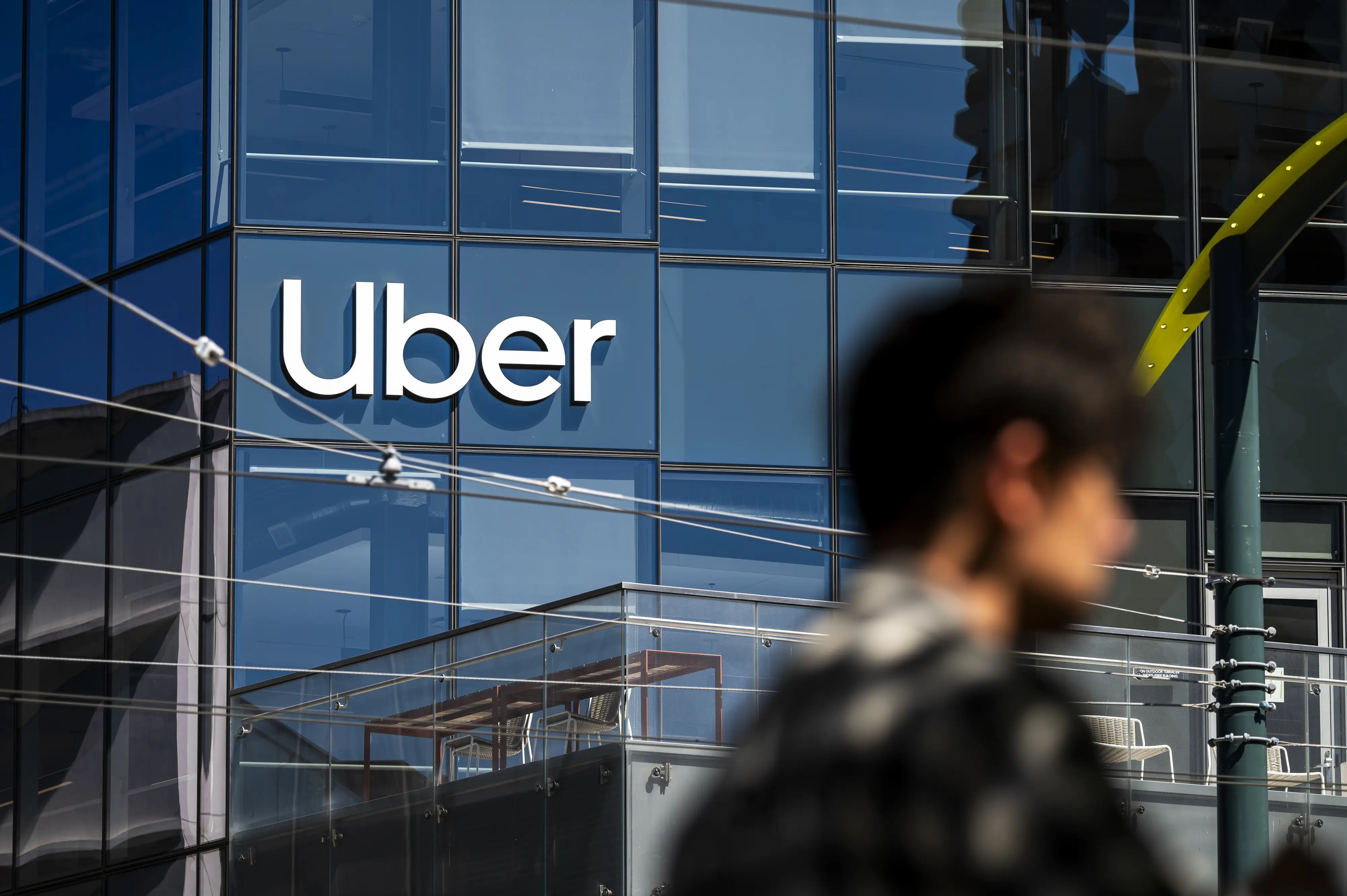 Uber logo displayed on a glass building facade with a blurred passerby in the foreground.