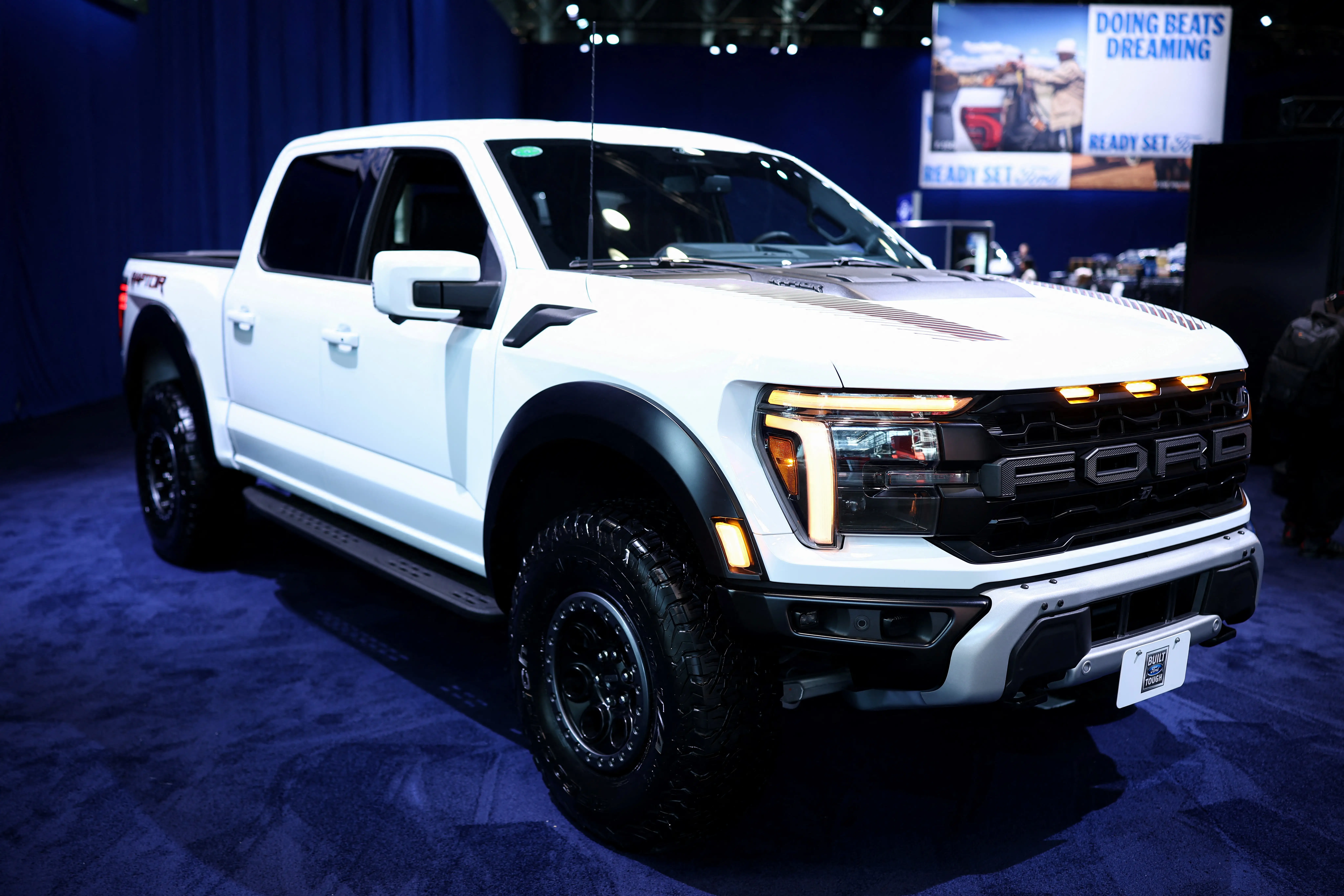 A white Ford F-150 Raptor on a showroom floor during an auto show.