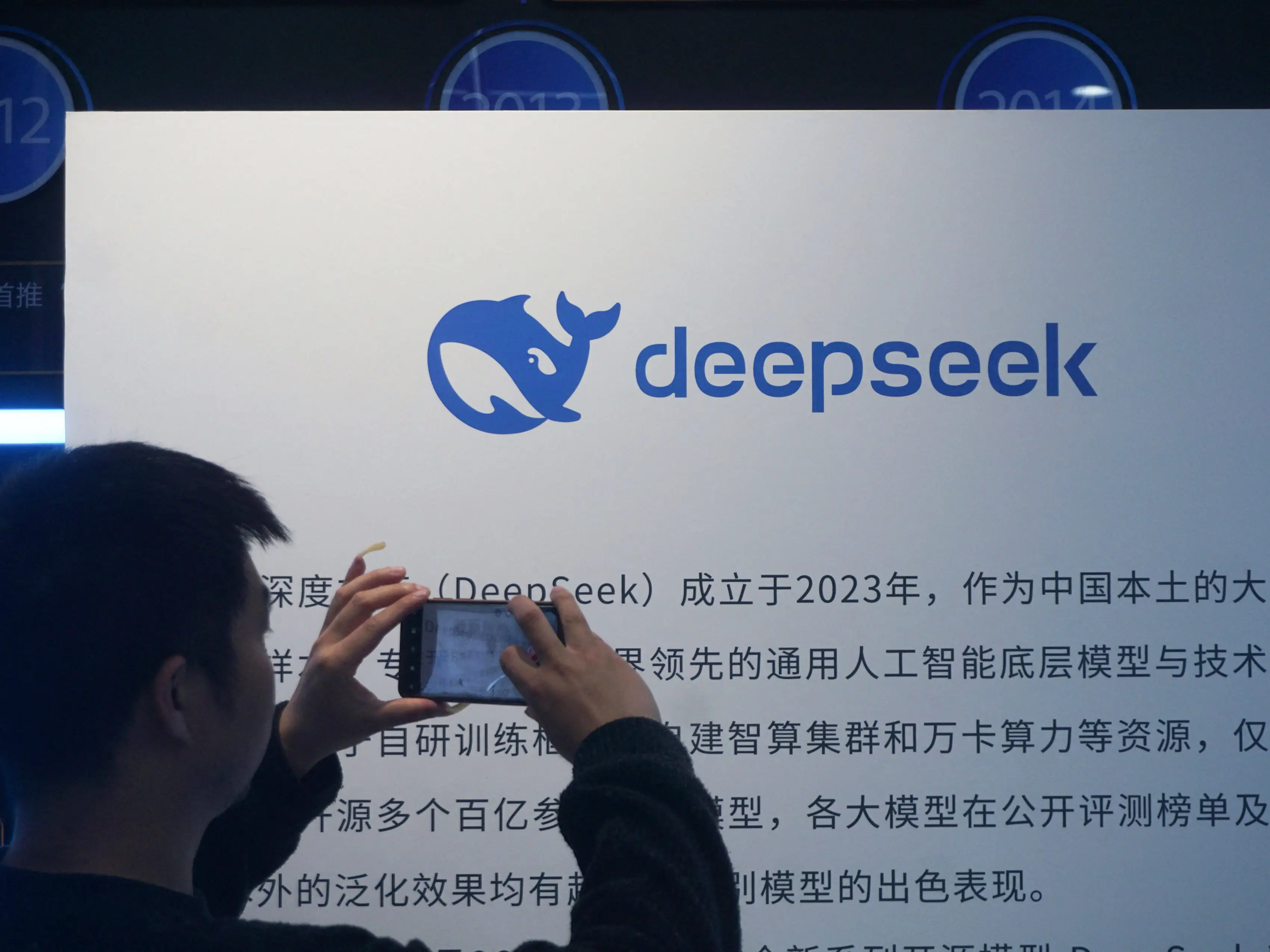 A man taking a photo of a DeepSeek display.