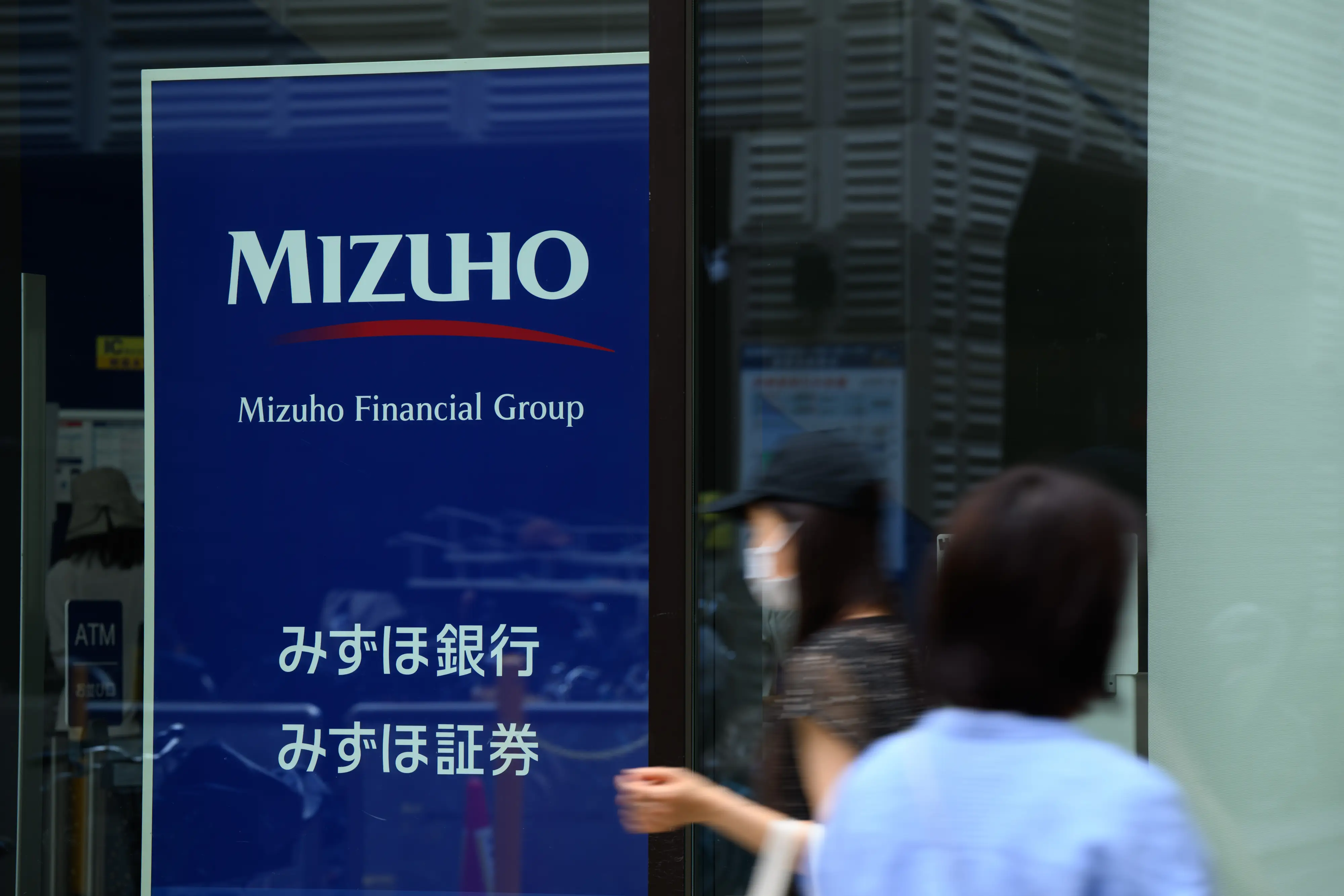 Pedestrians pass a MIZUHO storefront sign for Mizuho Financial Group with Japanese banking and securities text.