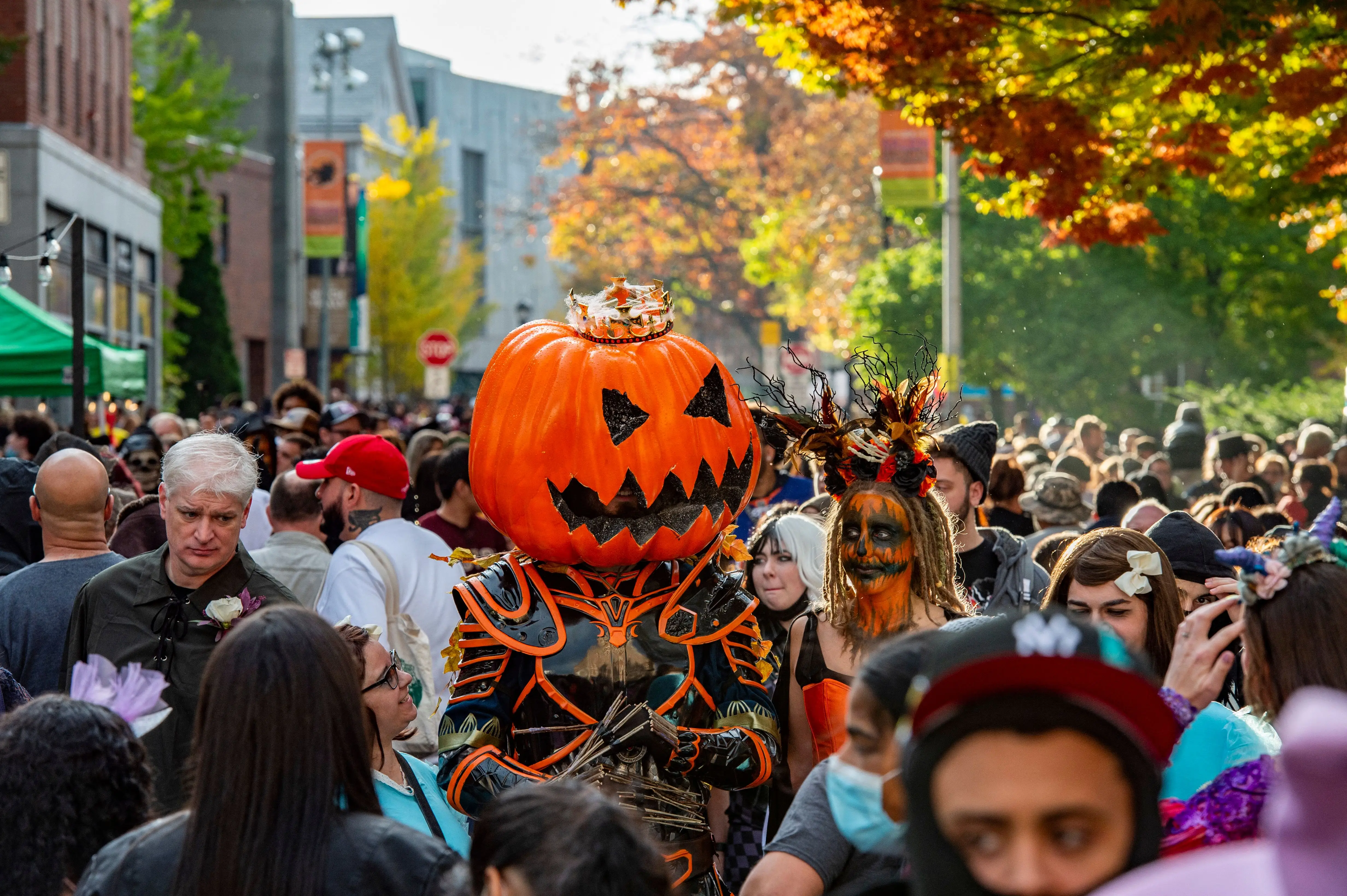 A large pumpkin-headed costumed reveller walks with others through a crowded street on Halloween in Salem, Massachusetts on October 31,