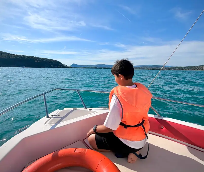 The writer's son sitting at the front of a boat, staring out at blue water in Lyon.