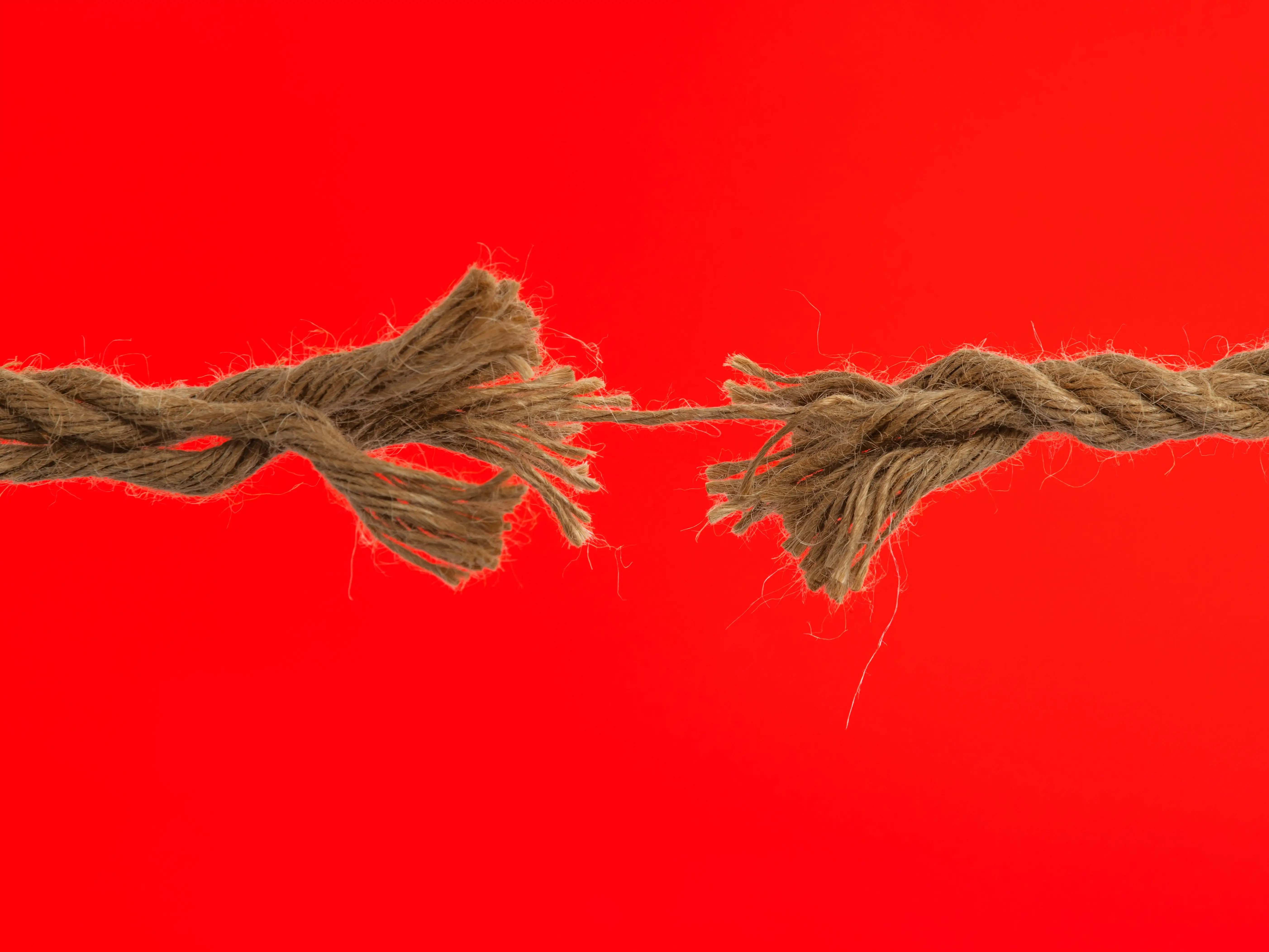 Frayed rope broken into two pieces against a bright red background.