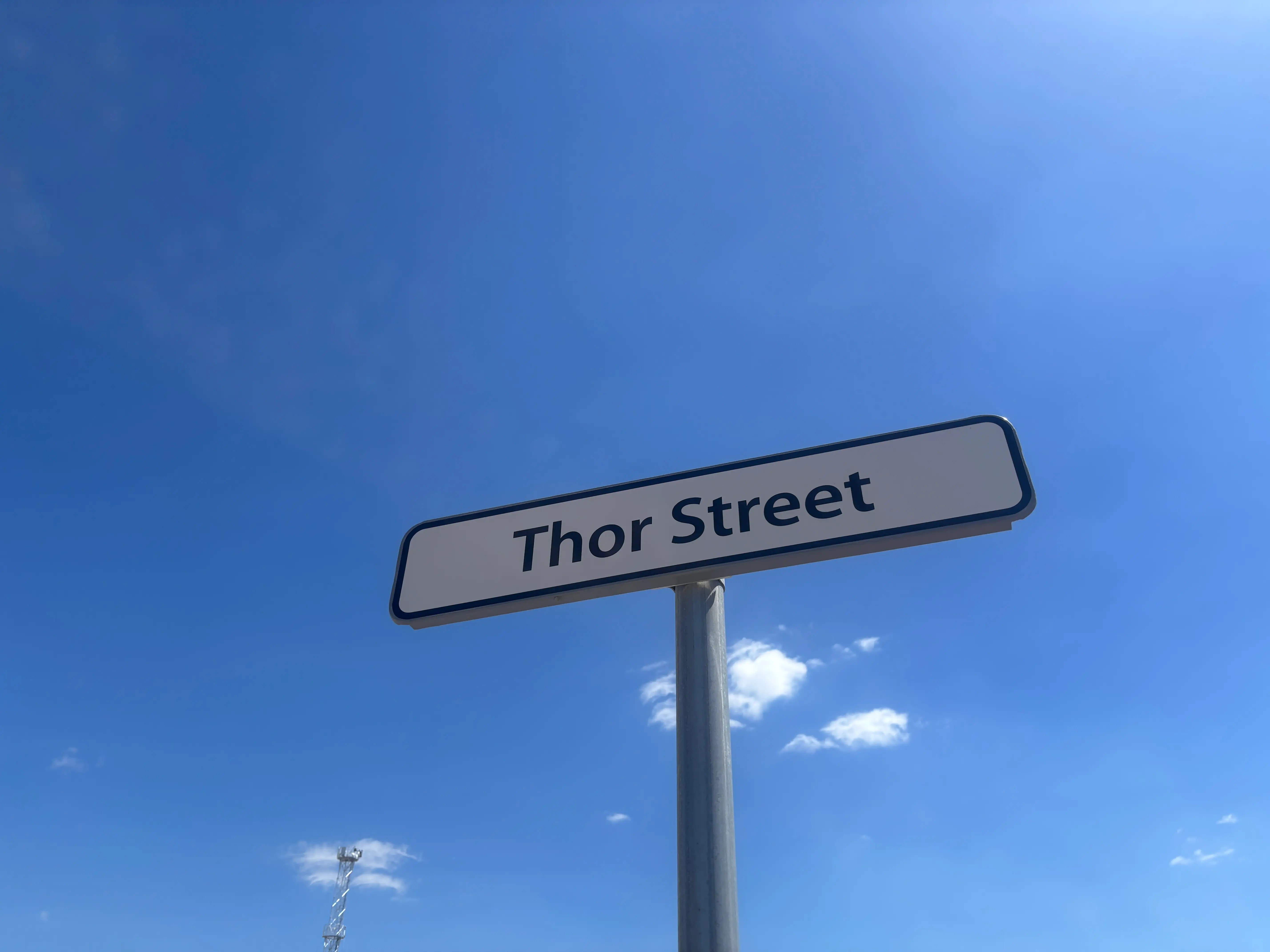 Thor Street road sign on a metal pole against a bright blue sky with small clouds.
