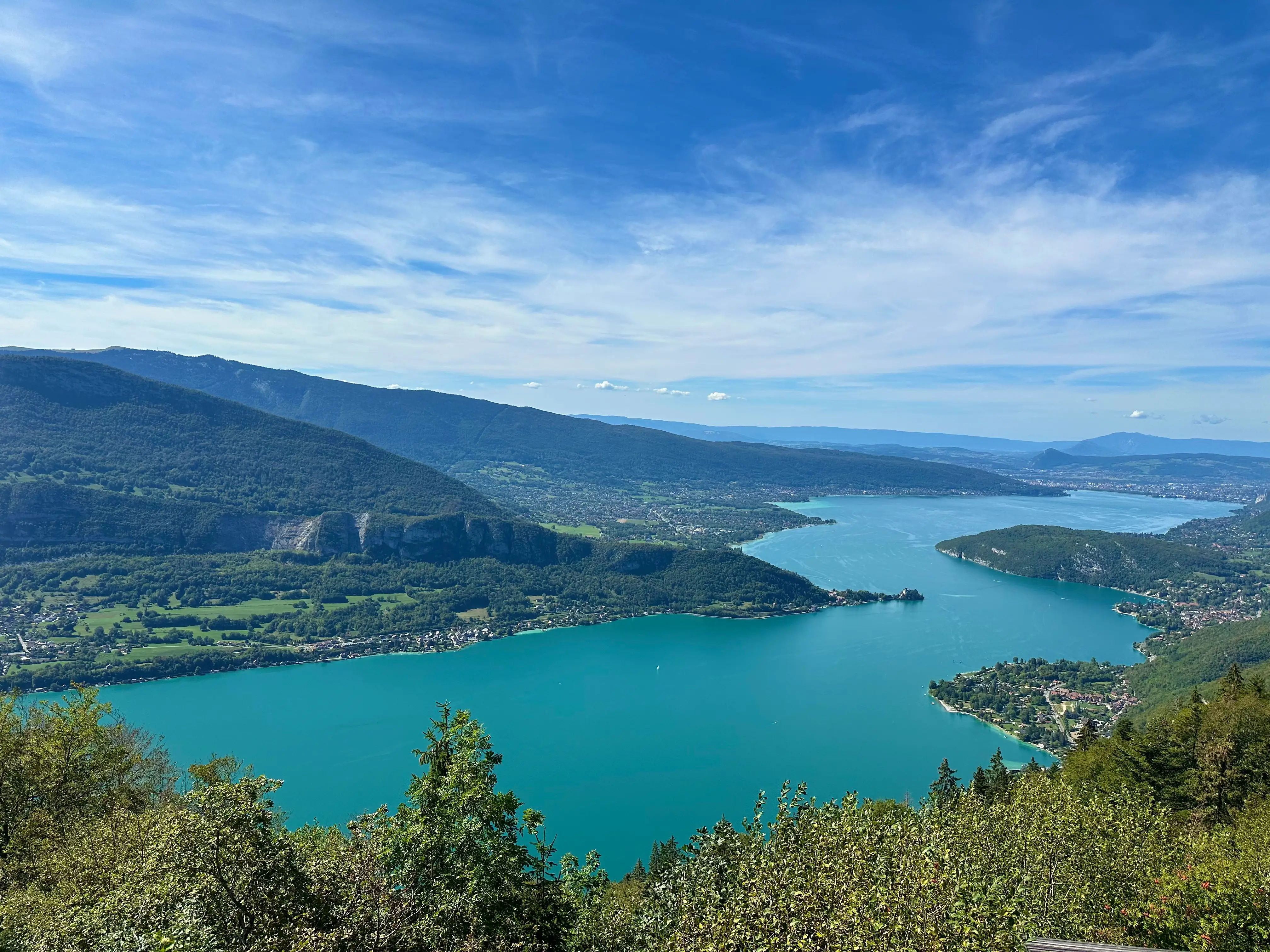 Turquoise alpine lake winds through forested mountains and lakeside villages under a blue sky.