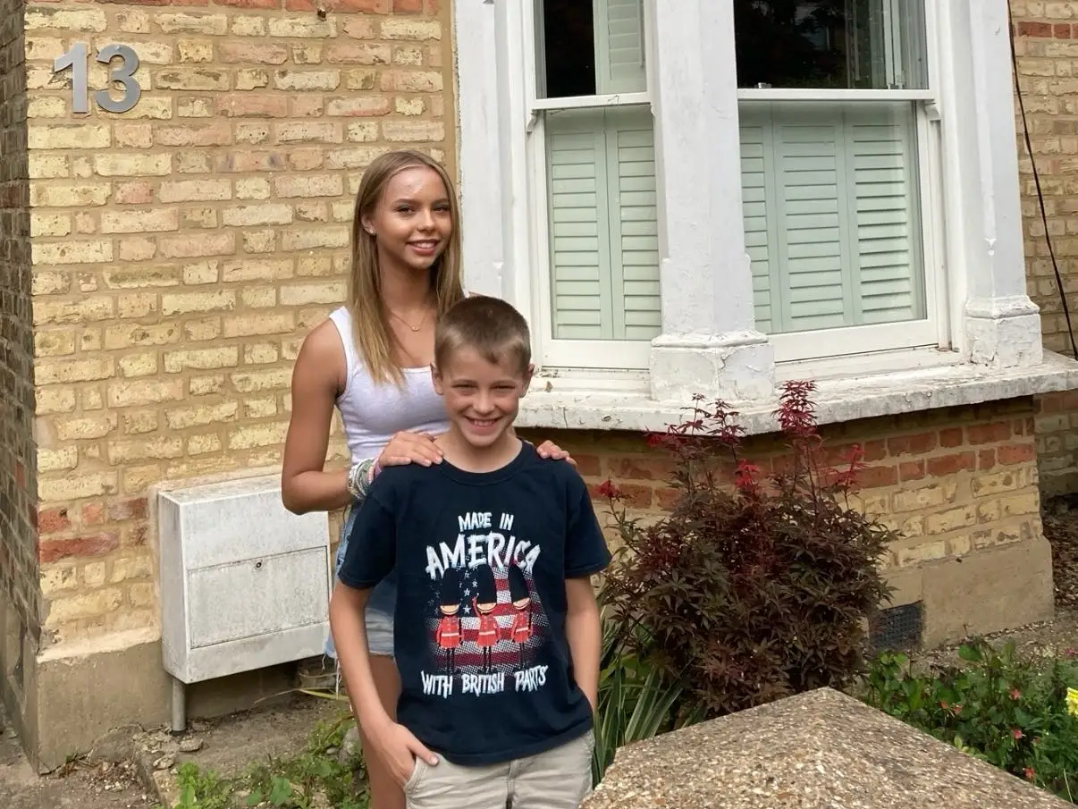 A brother and a sister standing outside a house.
