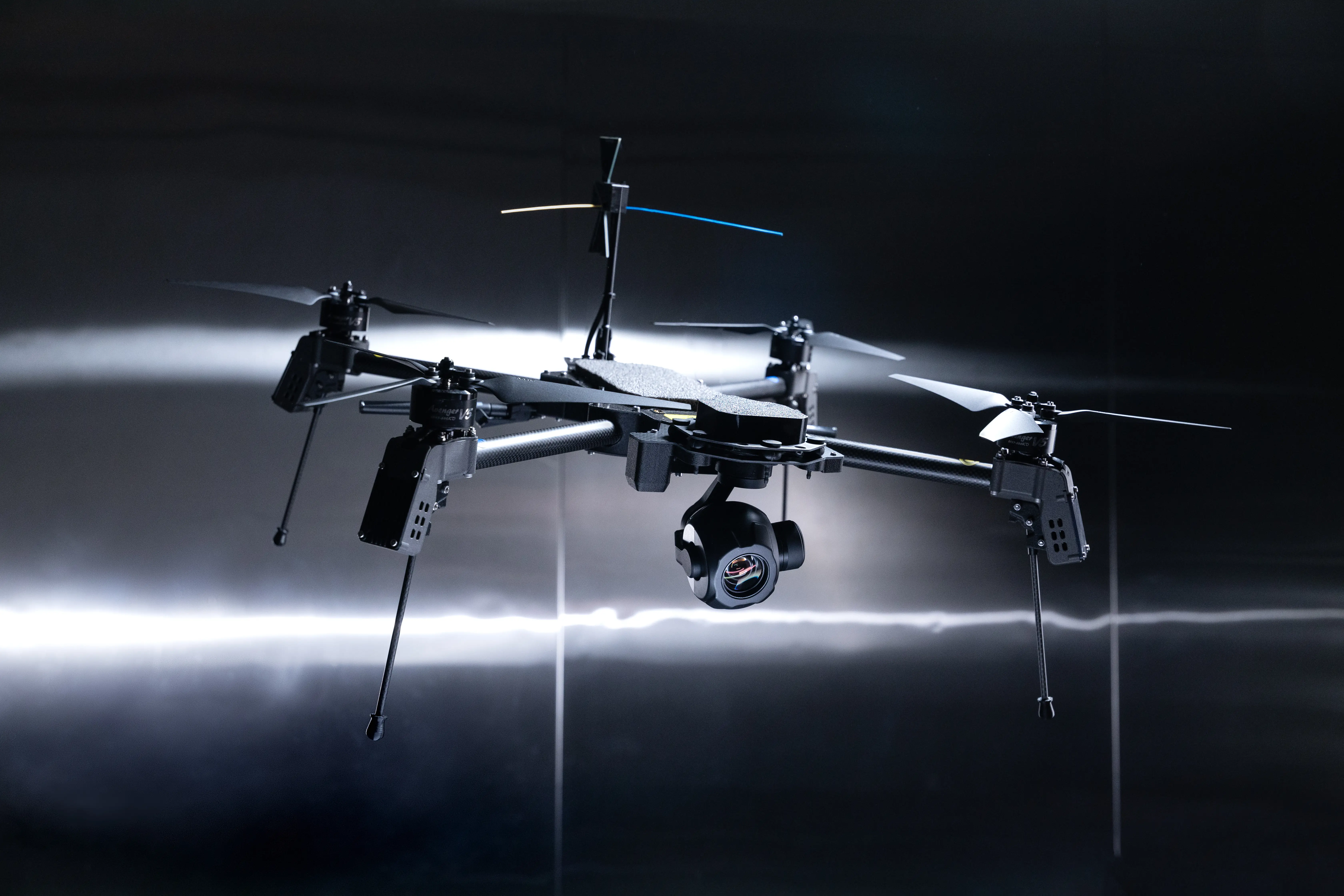 Black camera drone with spinning propellers hovers against a dark studio background with bright horizontal light streaks.