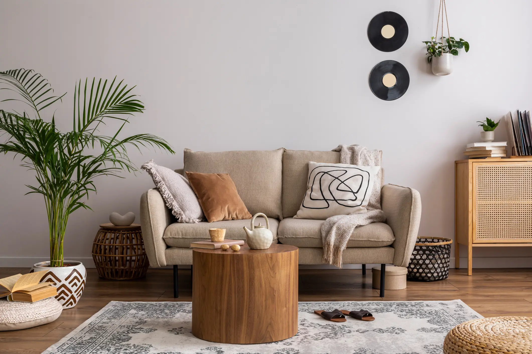 living room interior with beige sofa, carpet, pillow, plaid, coffee table and personal accessories. Beige wall.