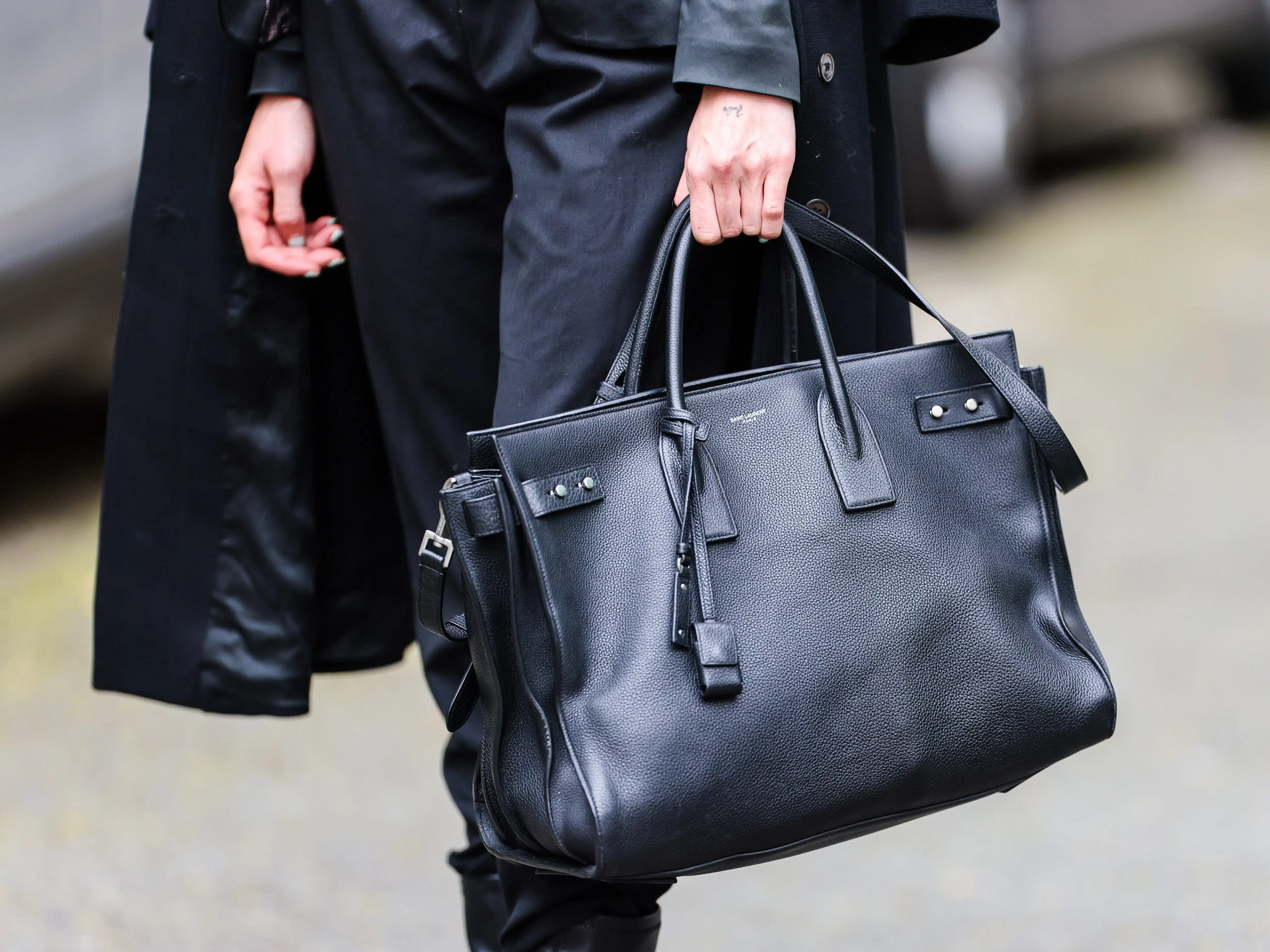 Cropped street-style view of a person carrying a large black leather handbag with an all-black outfit.
