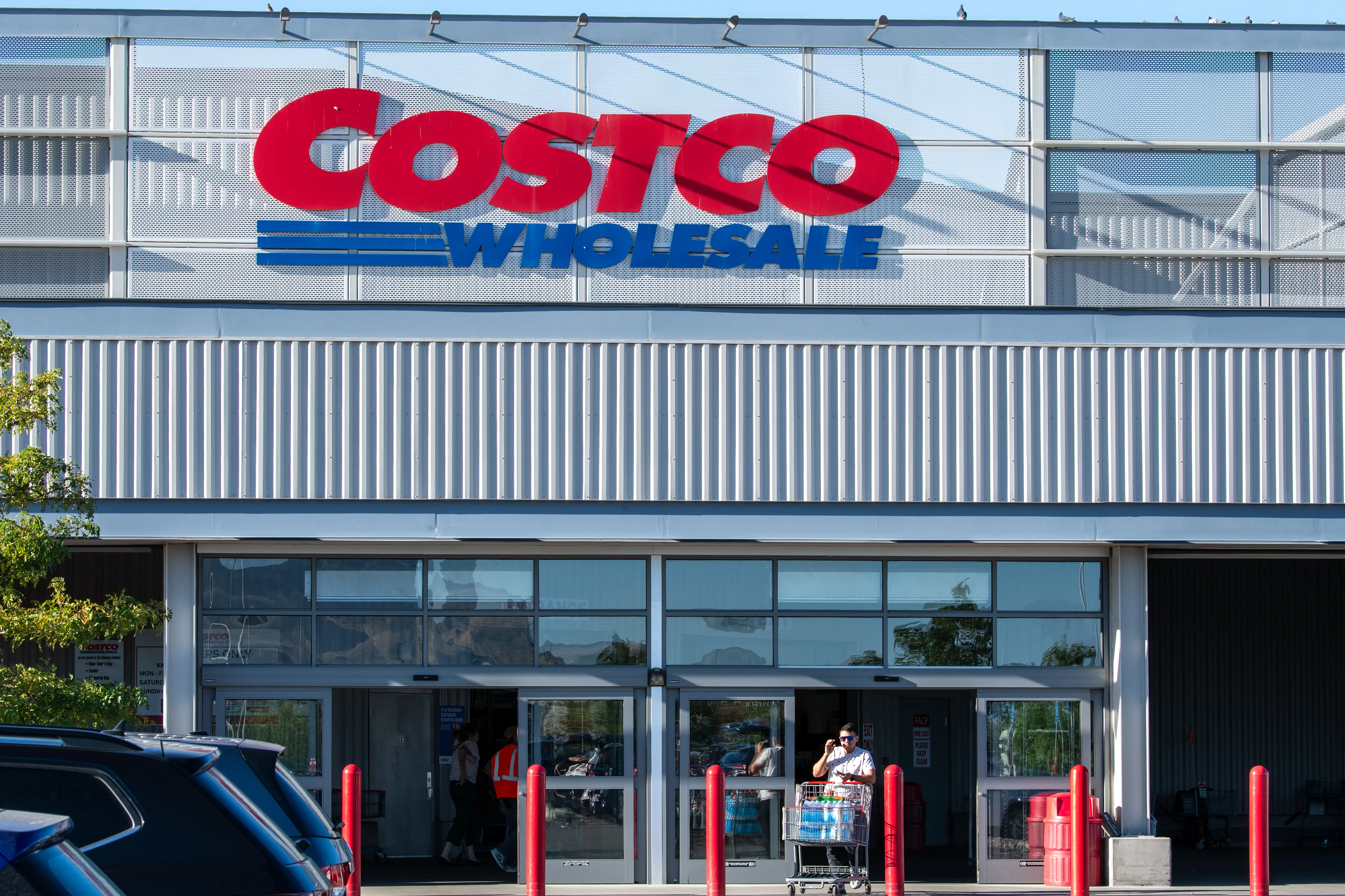 Costco Wholesale storefront with large red and blue sign above entrance doors and shoppers near carts.
