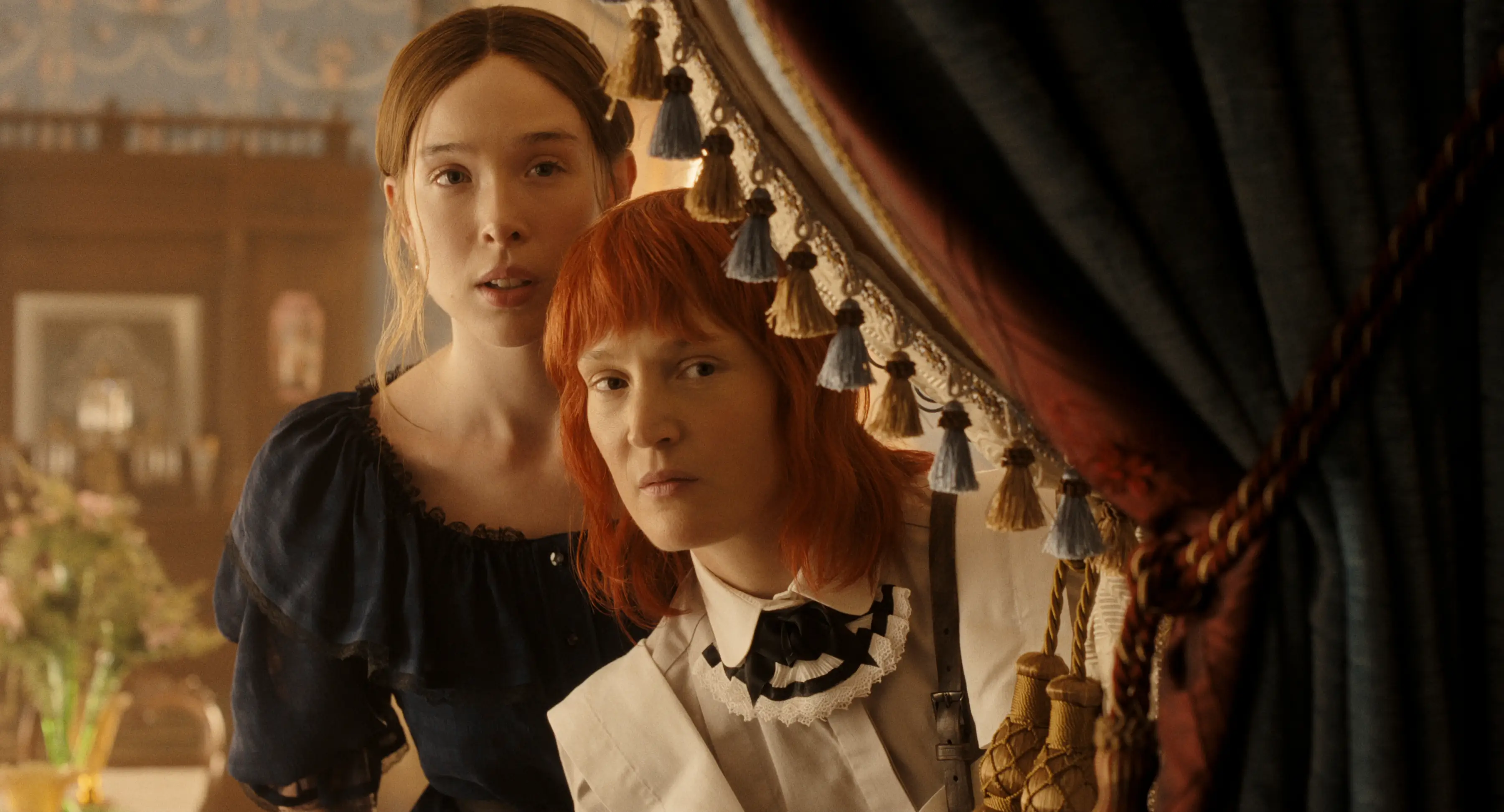 Ella Beatty and Vicky Krieps looking behind a curtain