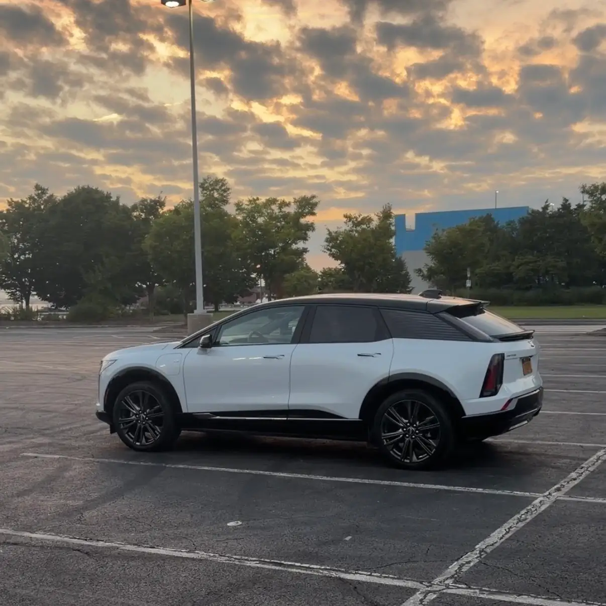 A white Cadillac Optiq is parked in a large parking lot at dusk.