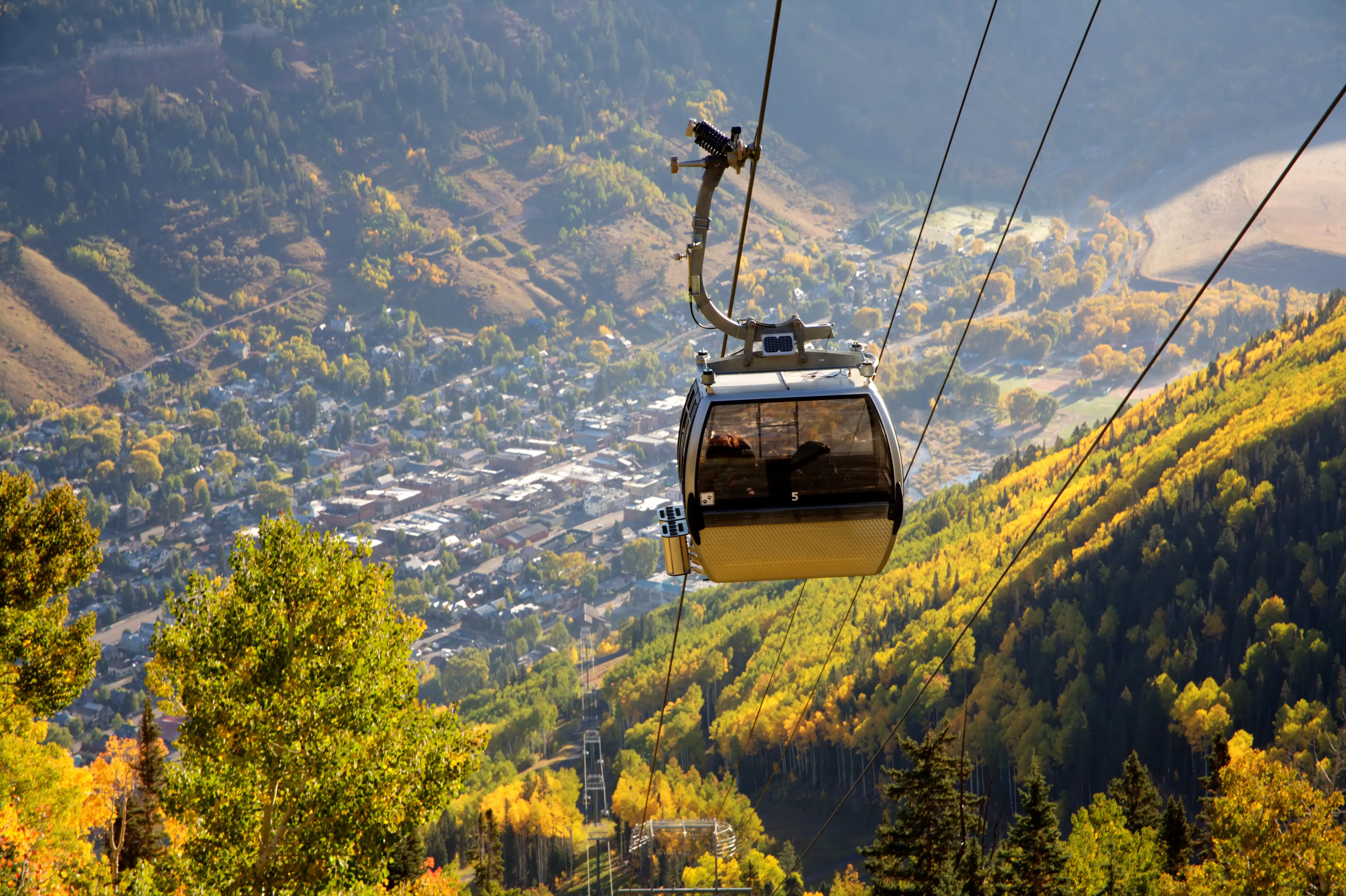 A gondola at Telluride Mountain in Colorado above green and yellow trees