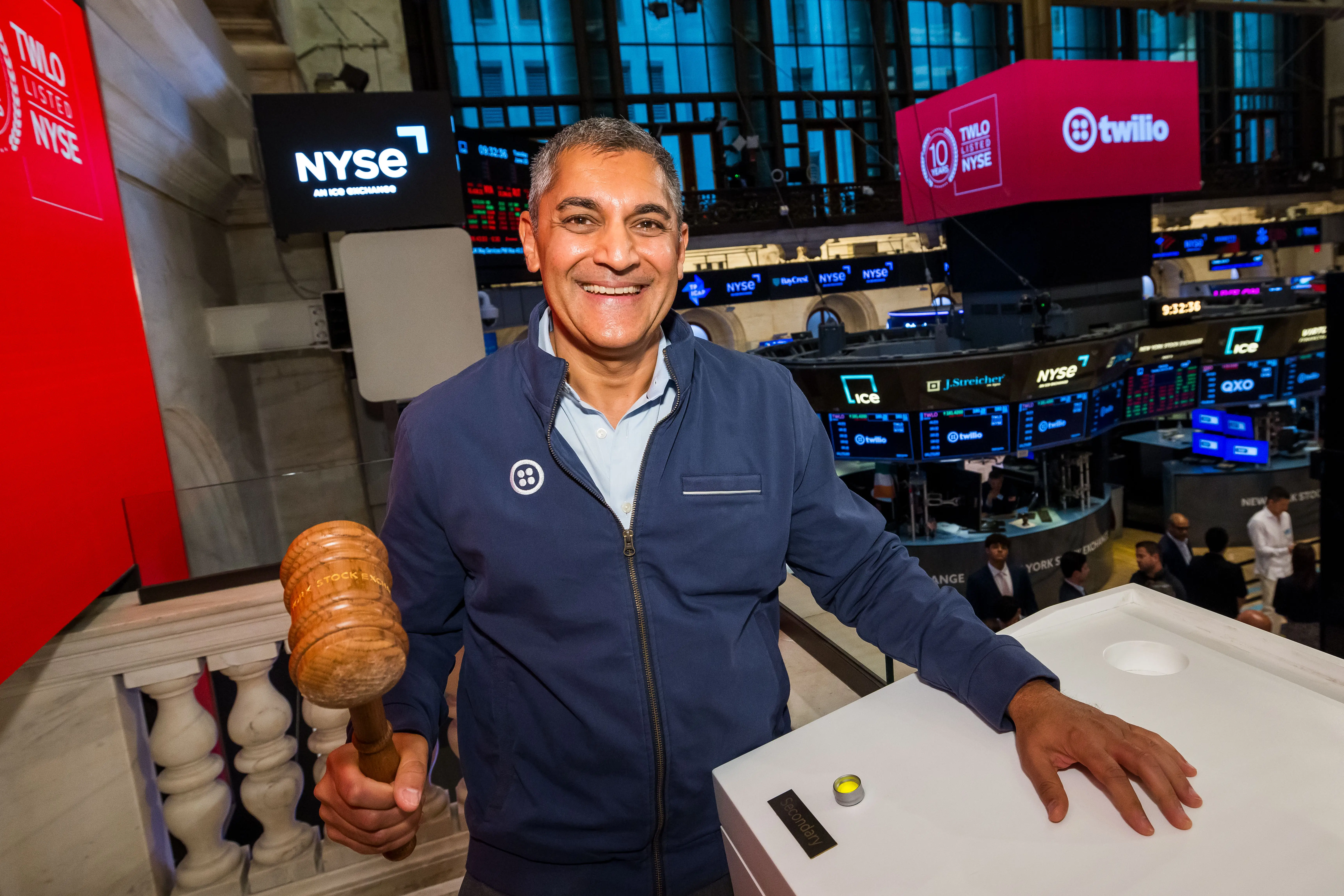 A CEO in a zip-up jacket and collar shirt, smiling and holding a gavel at the Nasdaq during a celebration of his company's 10-year anniversary since its IPO.