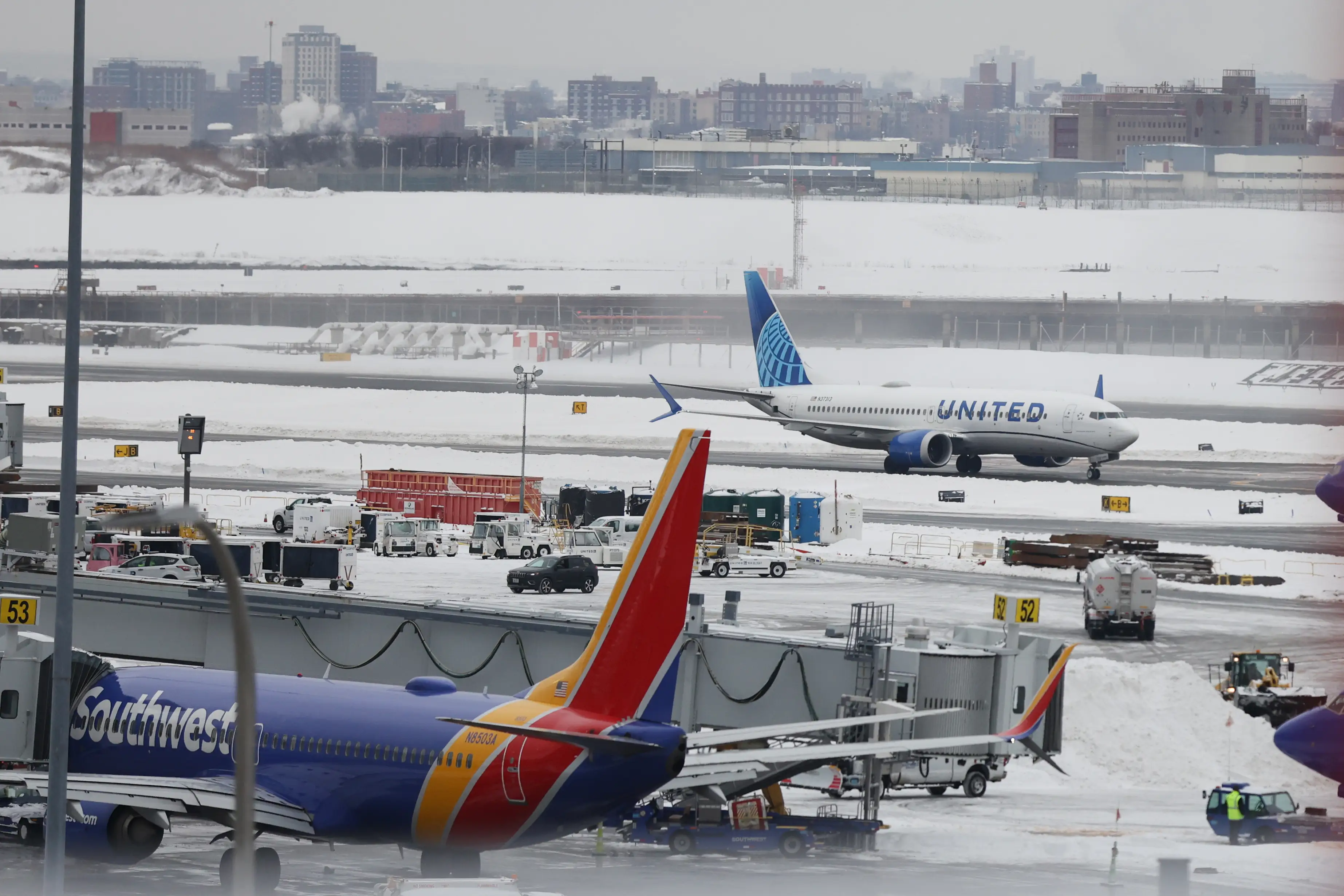 Snow-covered airport tarmac with Southwest aircraft at a gate and a United jet taxiing in the background.