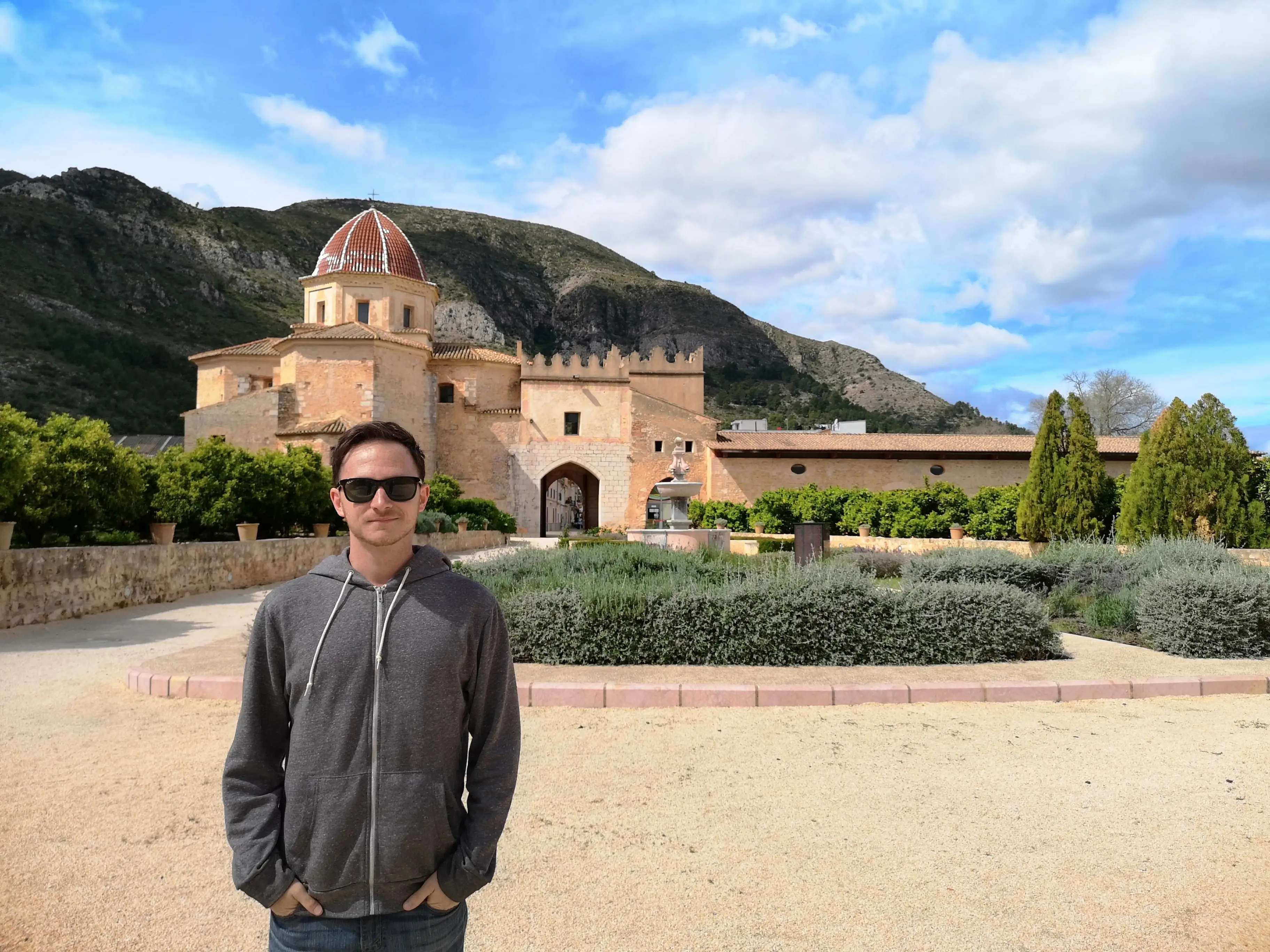 Kevin Joseph wearing sunglasses in a courtyard before a historic domed stone building in Simat de la Valldigna.
