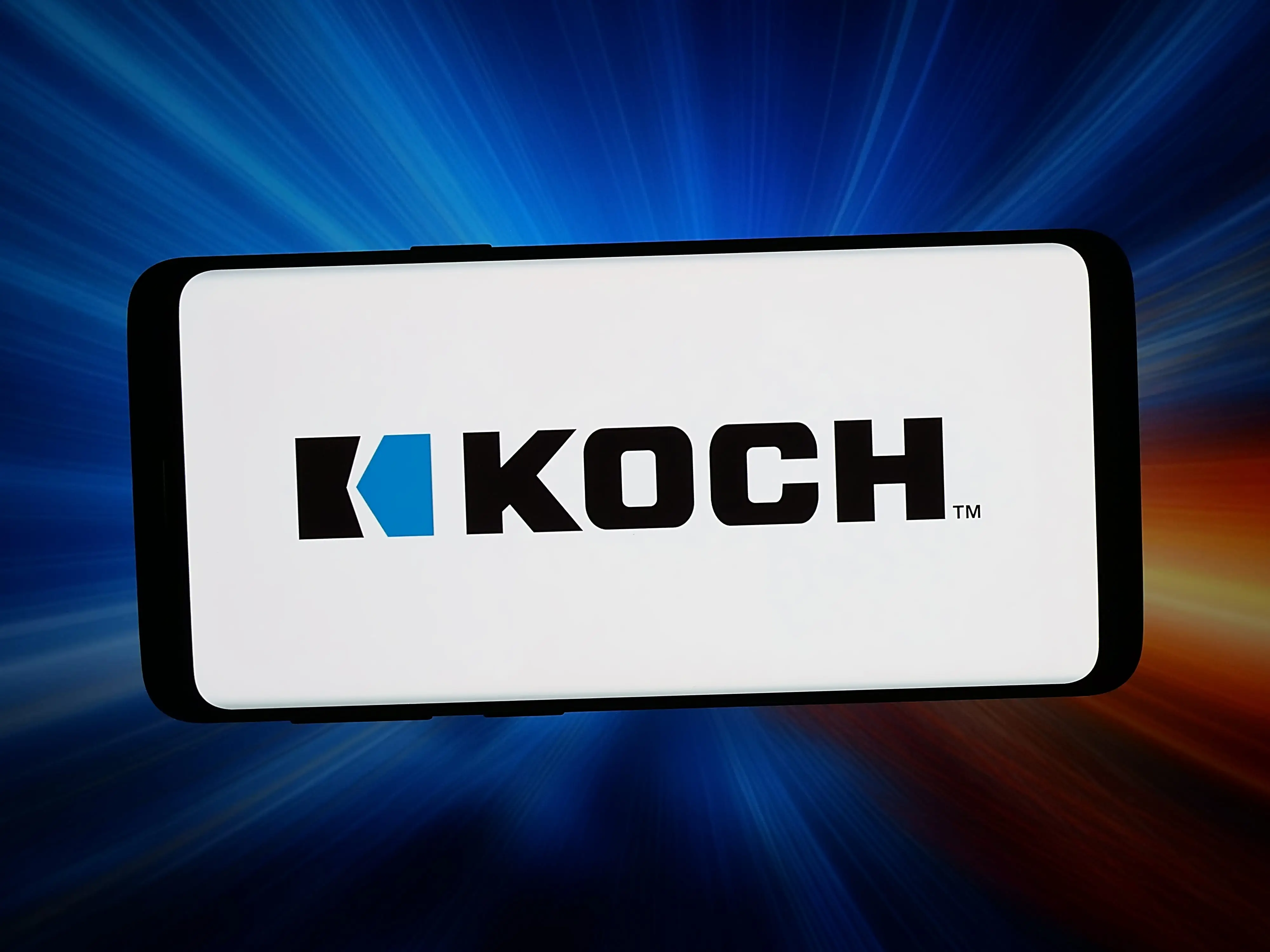 A smartphone displays the KOCH™ logo against a blue and red streaked light background.