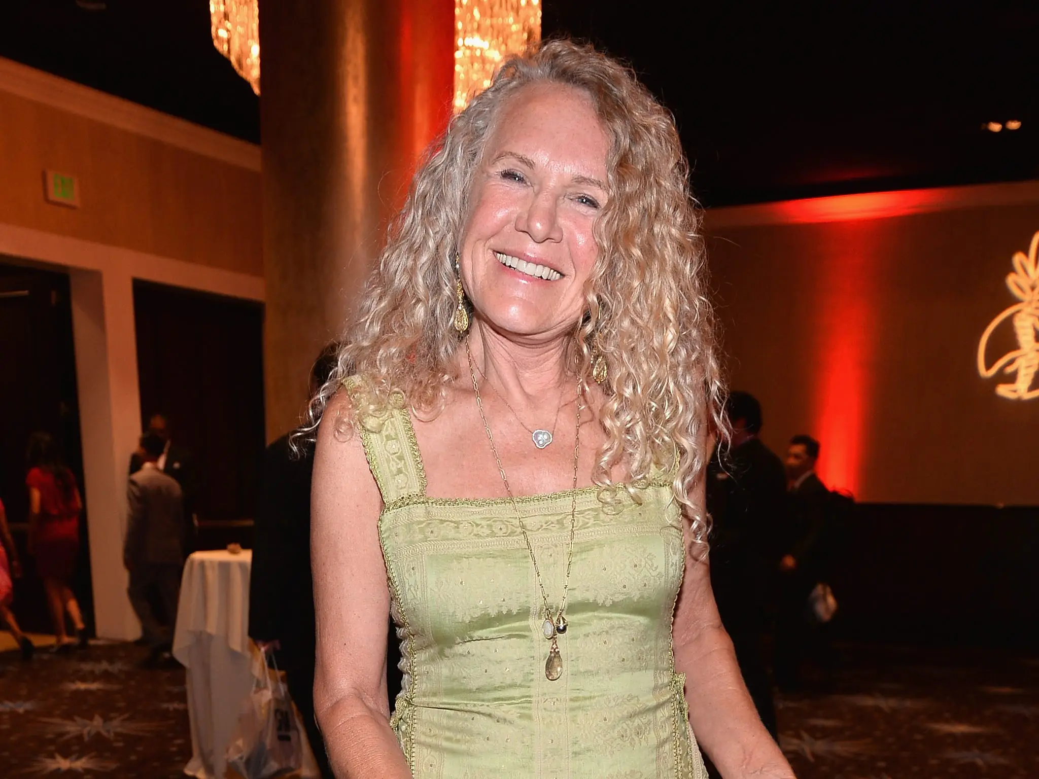 Christy Walton  smiles in a light green dress at an indoor event with patterned carpet and warm lighting.