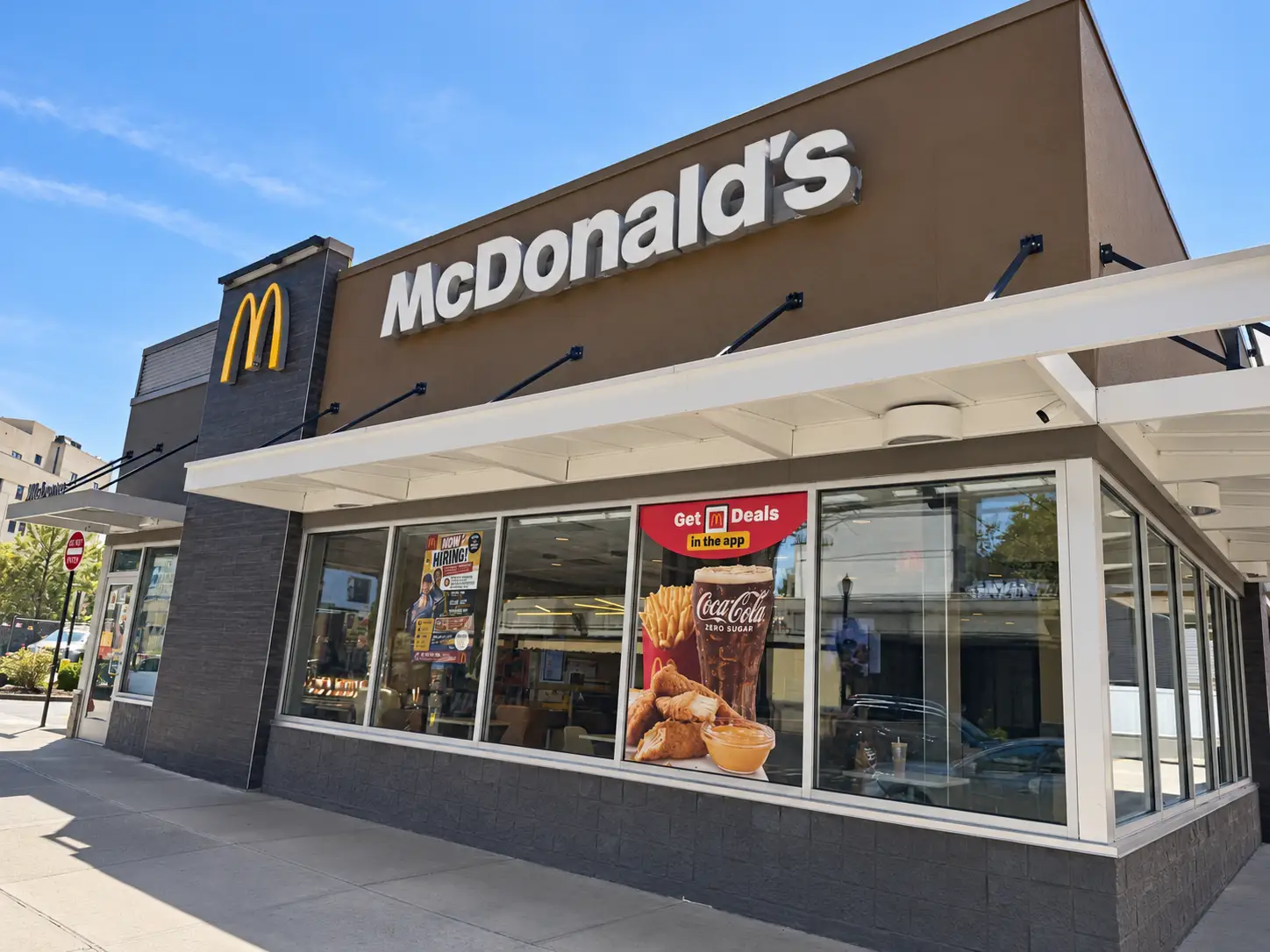 McDonald's restaurant exterior with large sign, golden arches, and promotional window posters along a city sidewalk.