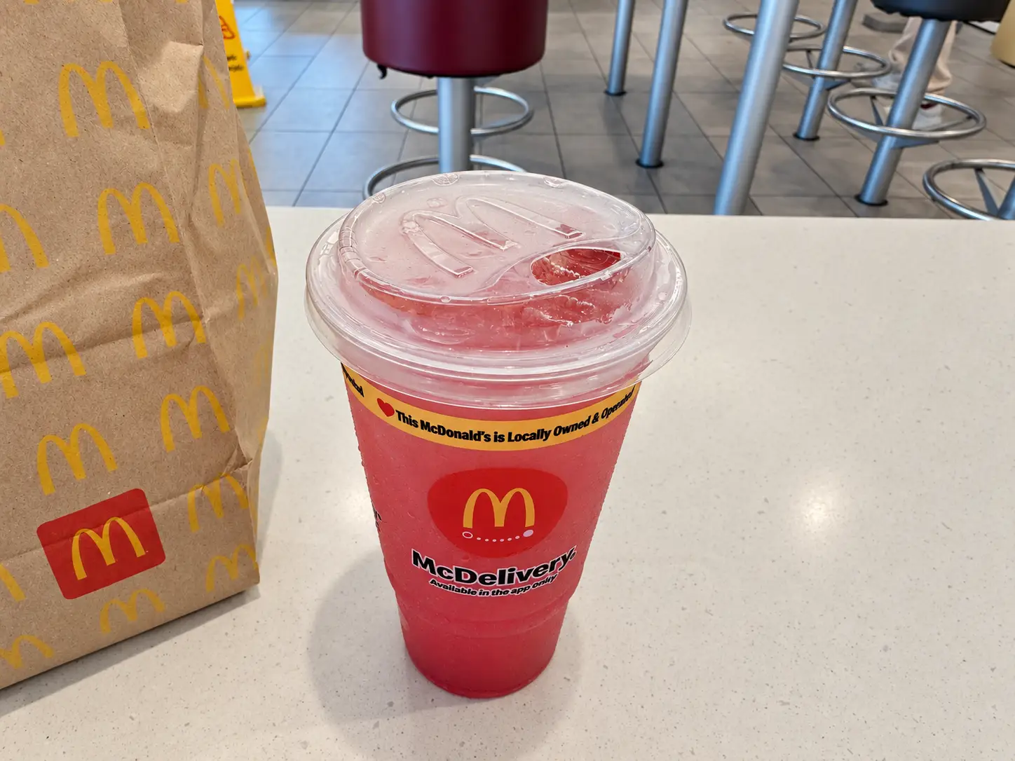 McDonald’s drink cup with red frozen beverage sits beside a branded paper bag on a restaurant counter.