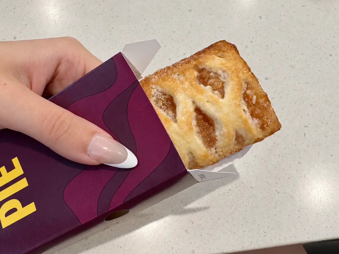A hand holds a McCafé PIE pastry partly pulled from a purple sleeve on a light countertop.