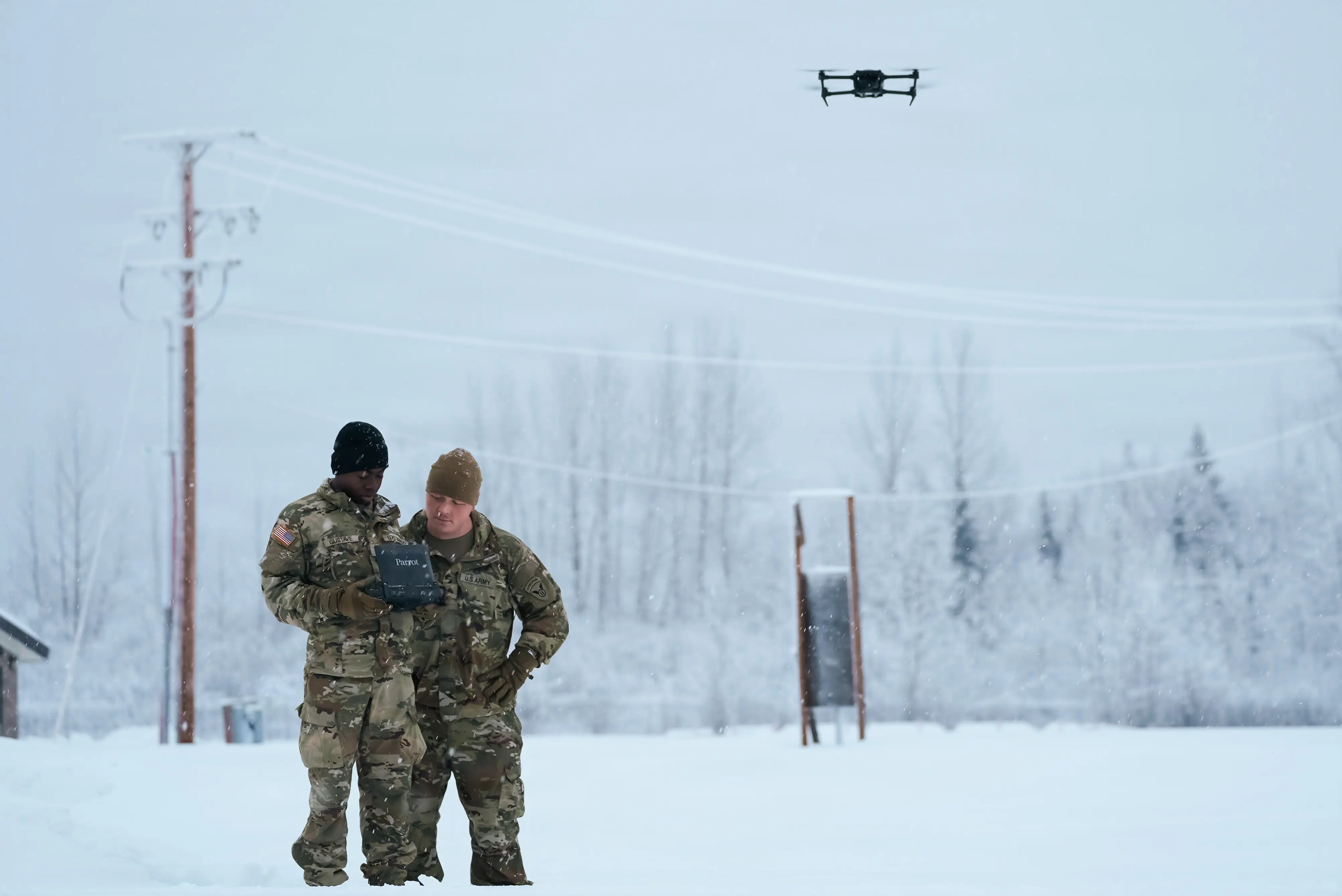 Two US Army soldiers stand in the snow flying a drone.