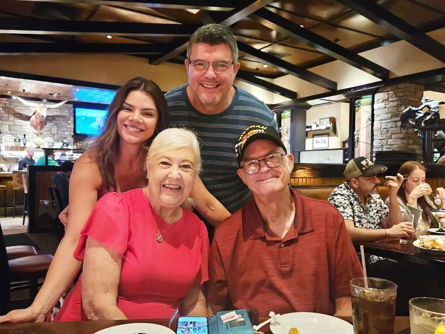 Four people pose smiling at a restaurant table with drinks and diners in the background.