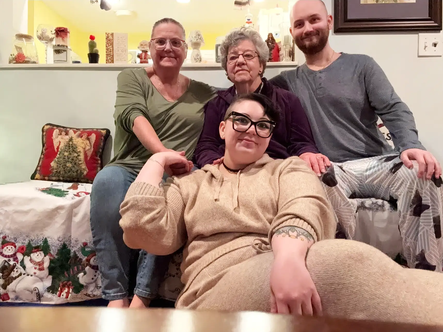 Four people sit together on a couch in a warmly lit room with holiday decorations.
