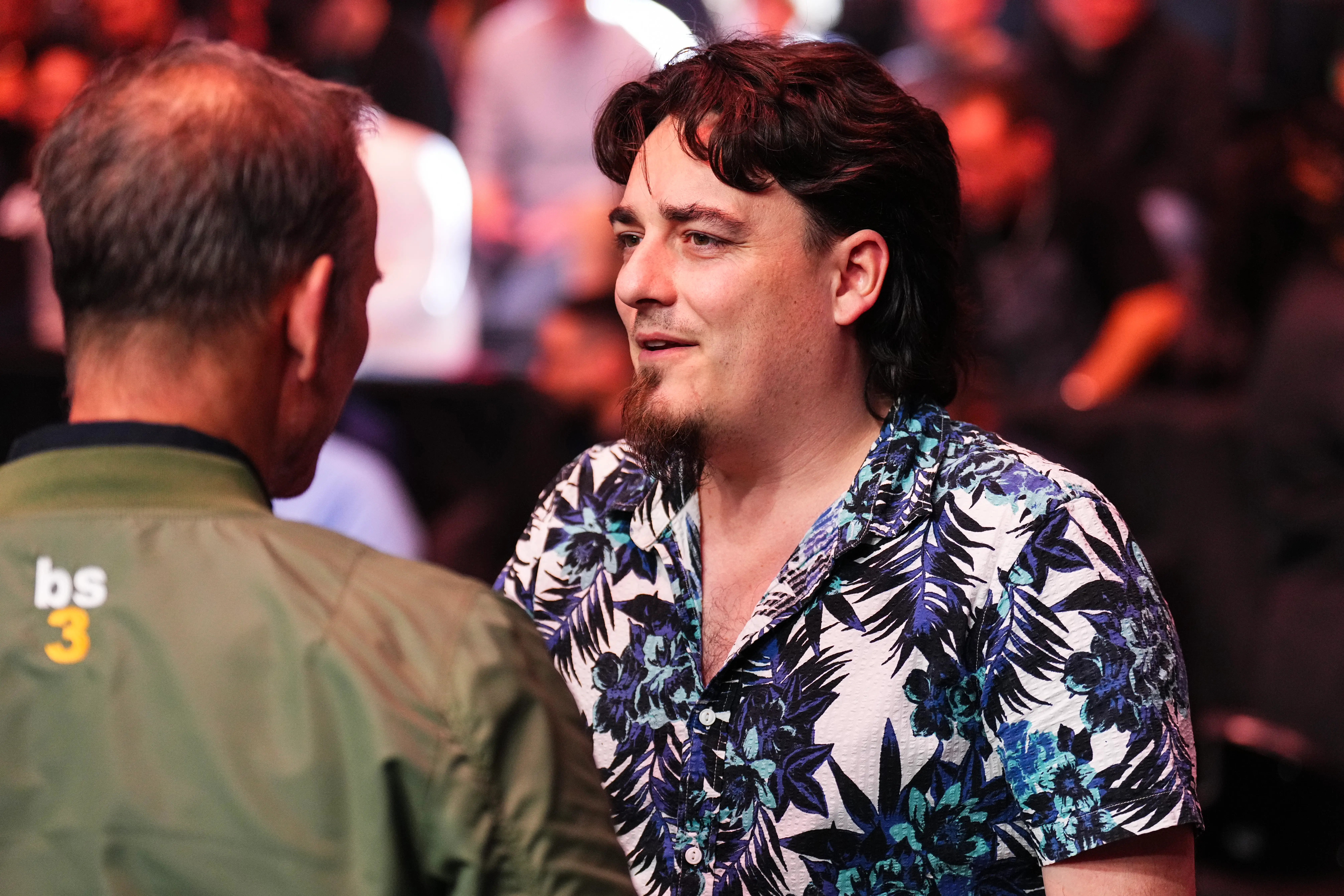 A man in a Hawaiian shirt speaks to another person.
