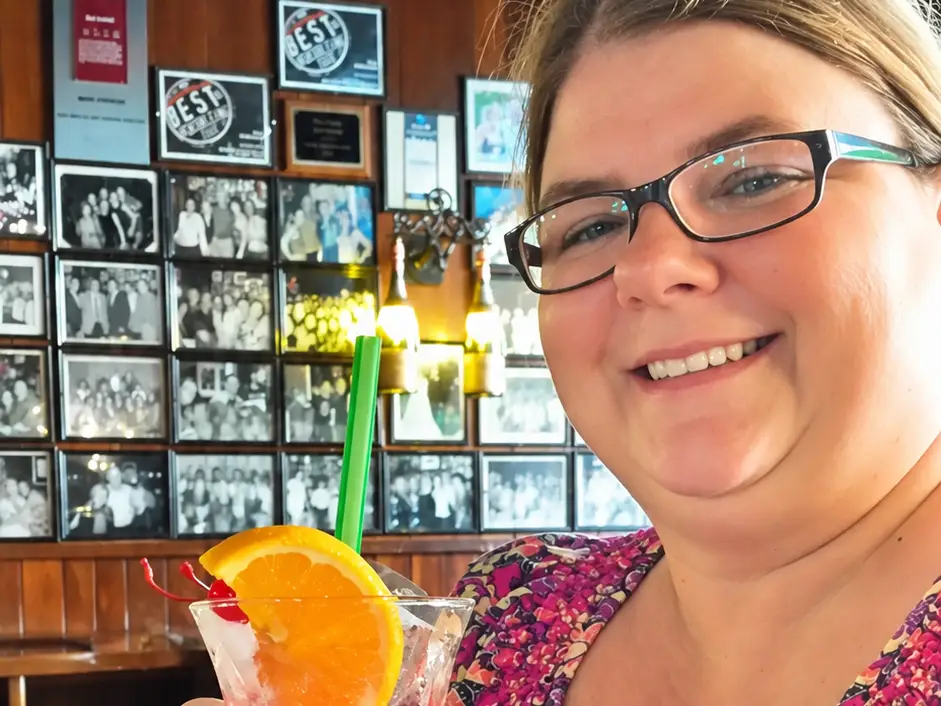 A woman wearing a pink patterned dress with a cocktail in her hand.