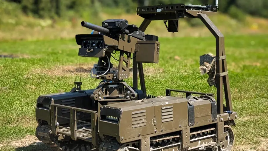 Tracked robotic ground vehicle with a mounted weapon system stands on grass in an outdoor field.