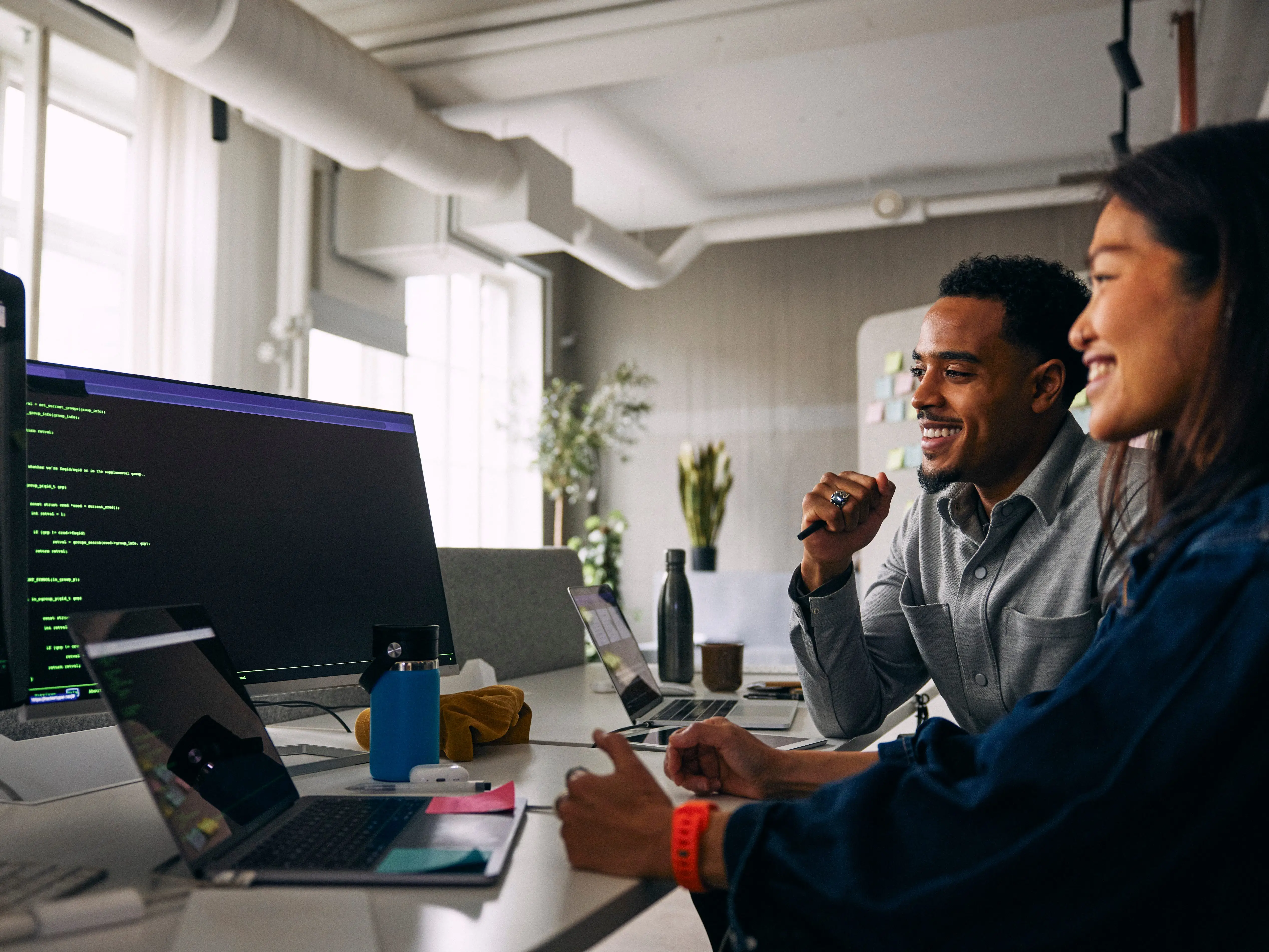 Two people at a desk with laptops and monitors in an office