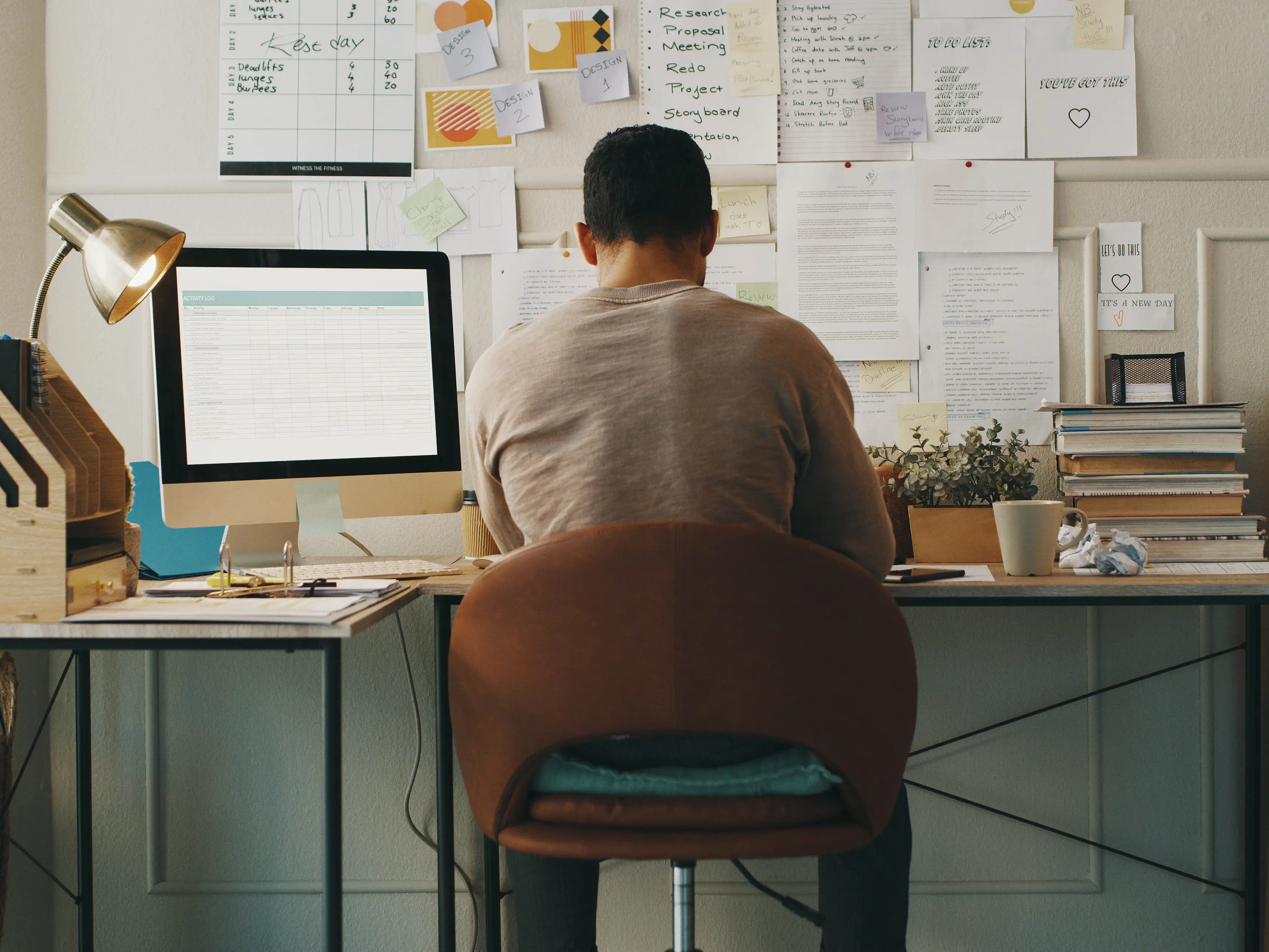 a man working at a computer with papers taped to the wall in front of his desk