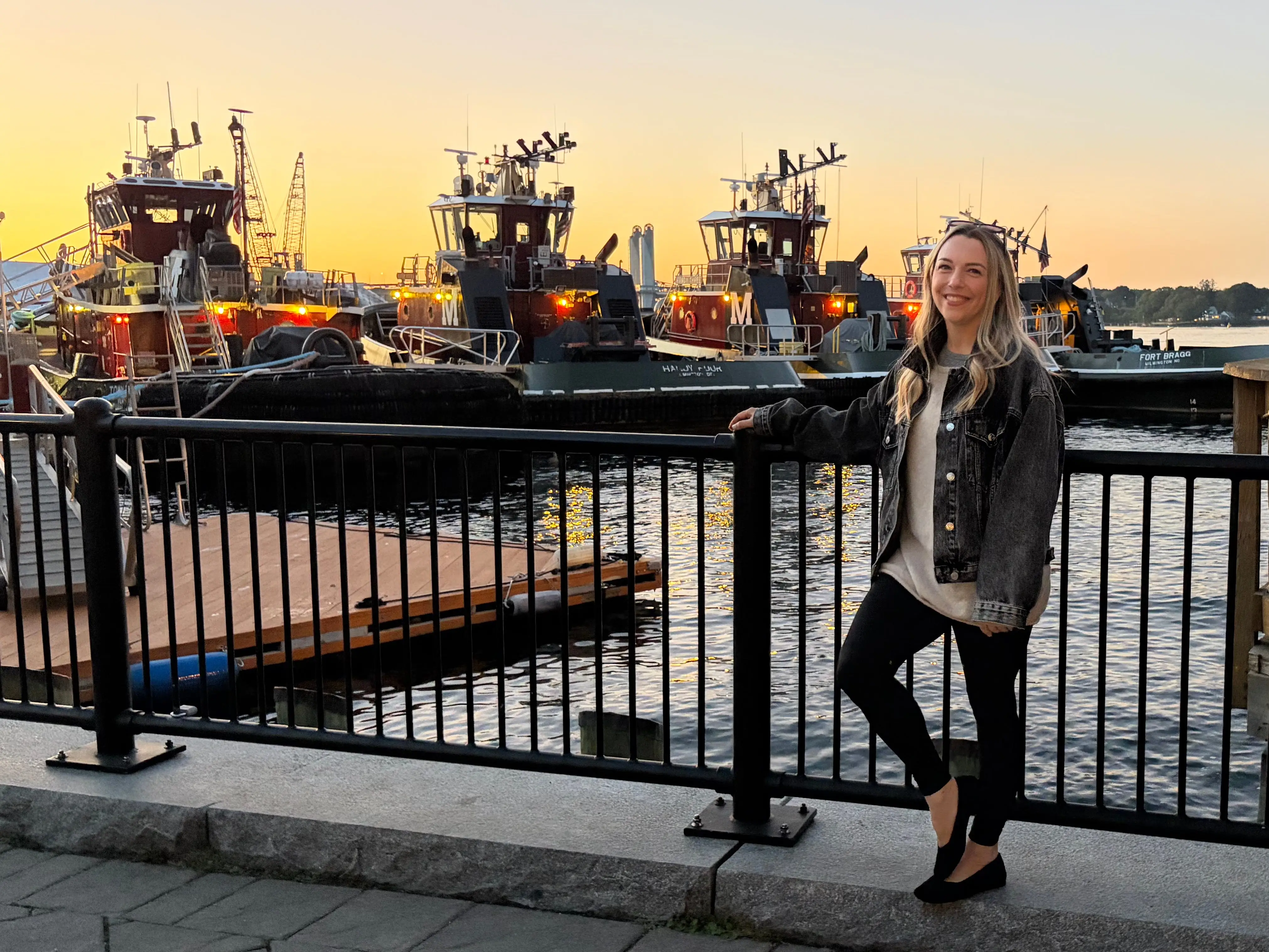Rebecca poses near boats at sunset.
