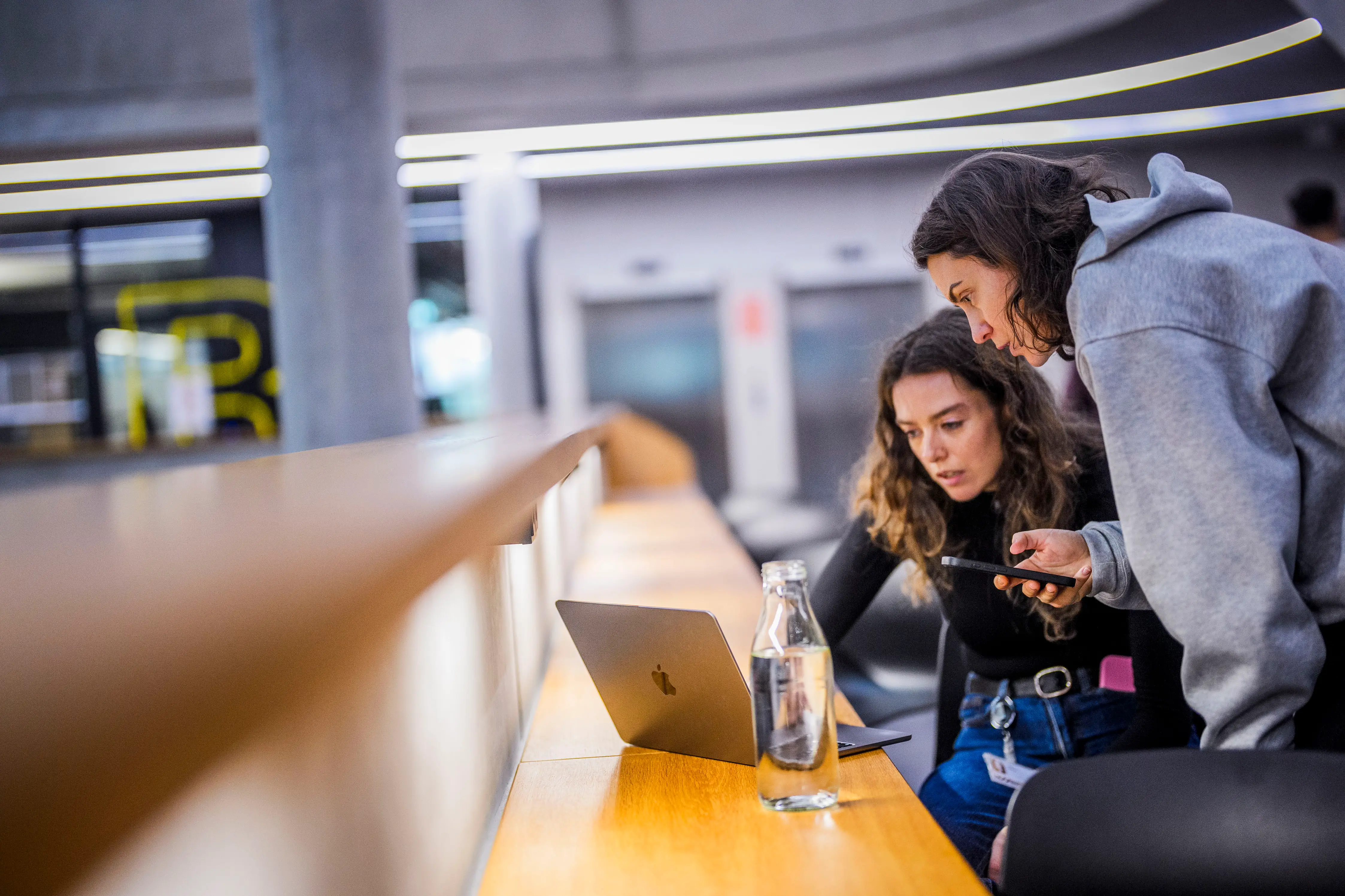 Two women look at a smartphone and a laptop