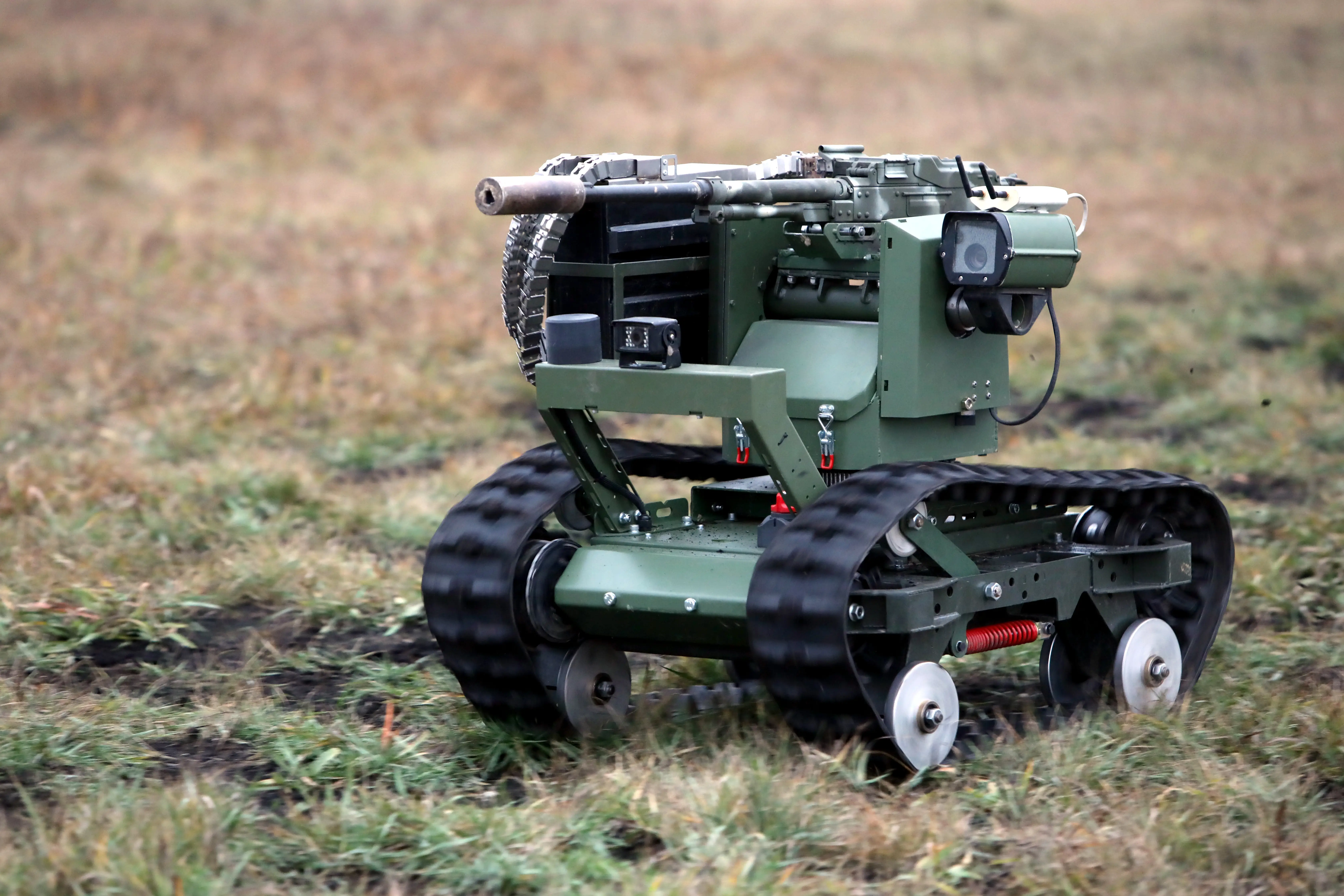 Tracked military robot with a mounted weapon moves across a grassy field.