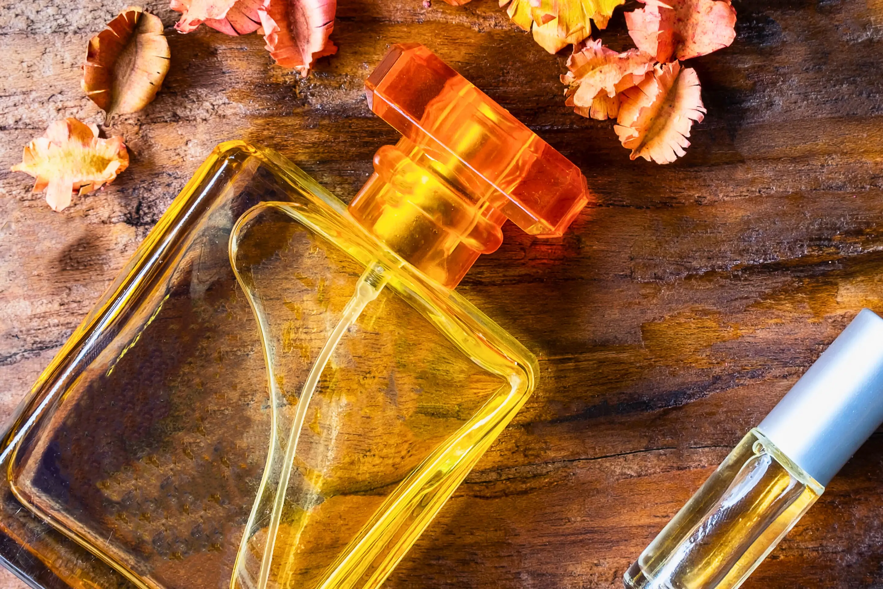 Two perfume bottles rest on a wooden surface with orange pencil shavings scattered around them.