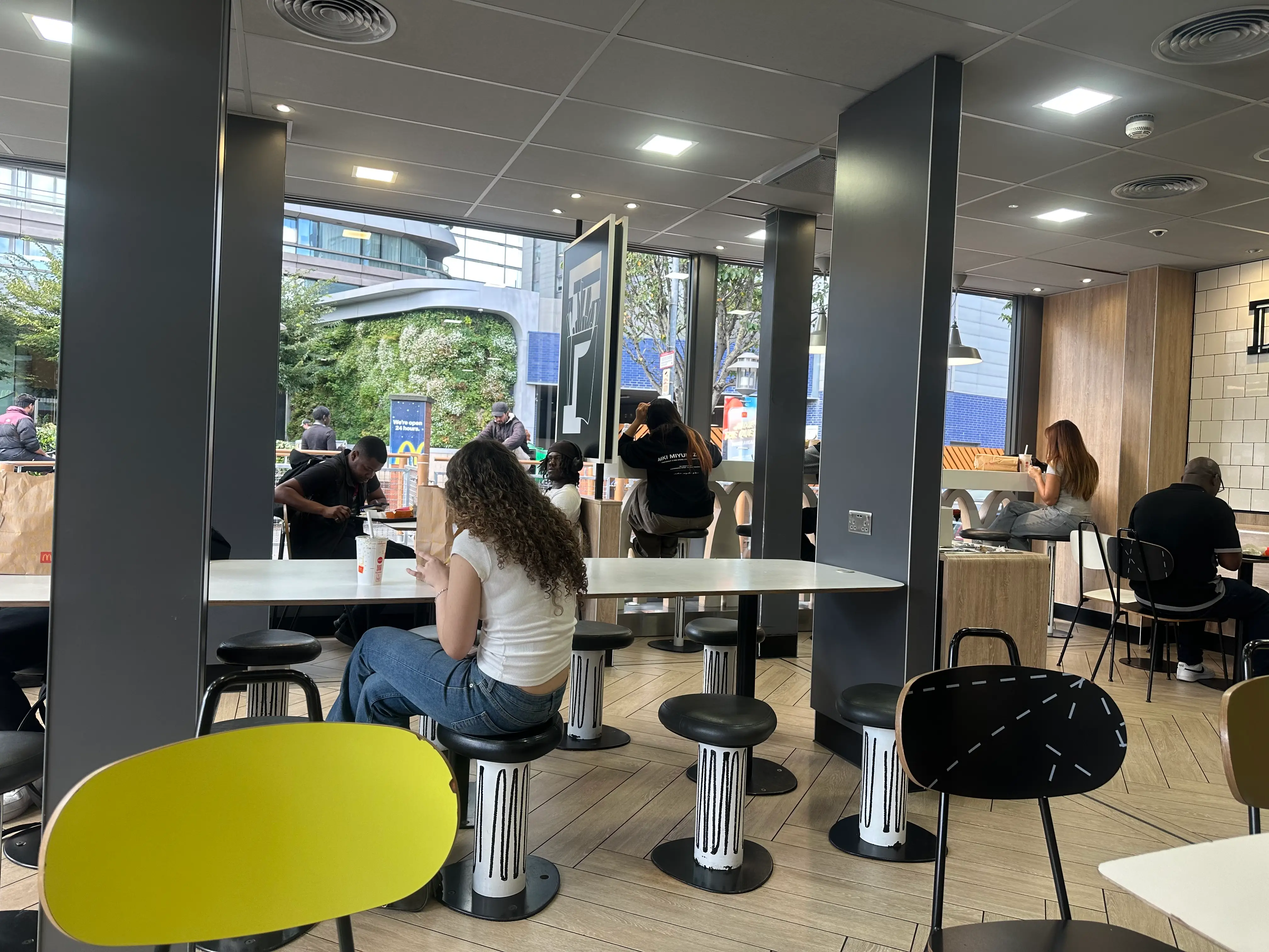 Customers sit at tables inside a McDonald's restaurant with modern seating, large windows, and street views outside.