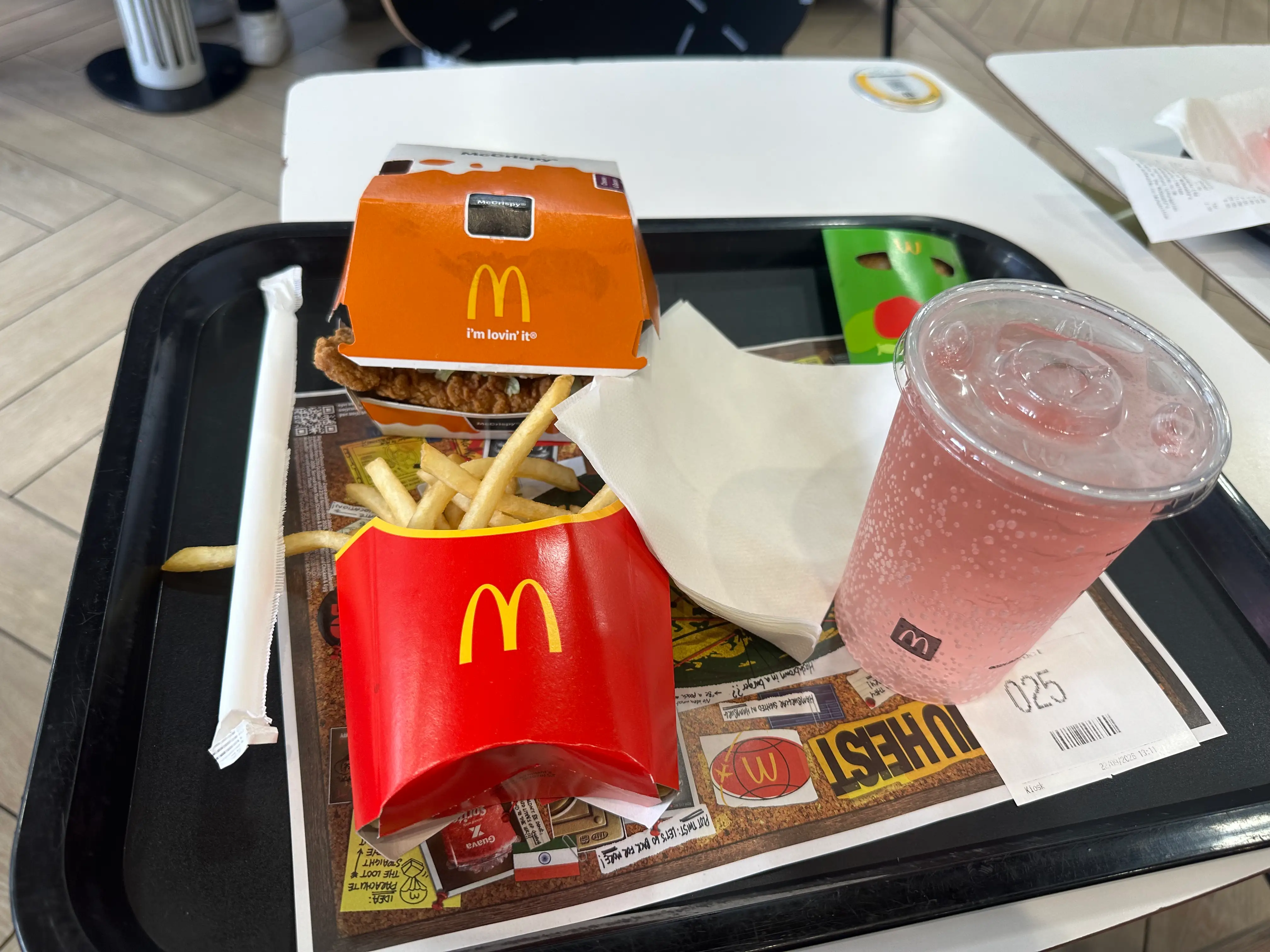 McDonald's fries, a sandwich box, a pink soft drink, and a receipt sit on a black tray in a restaurant.